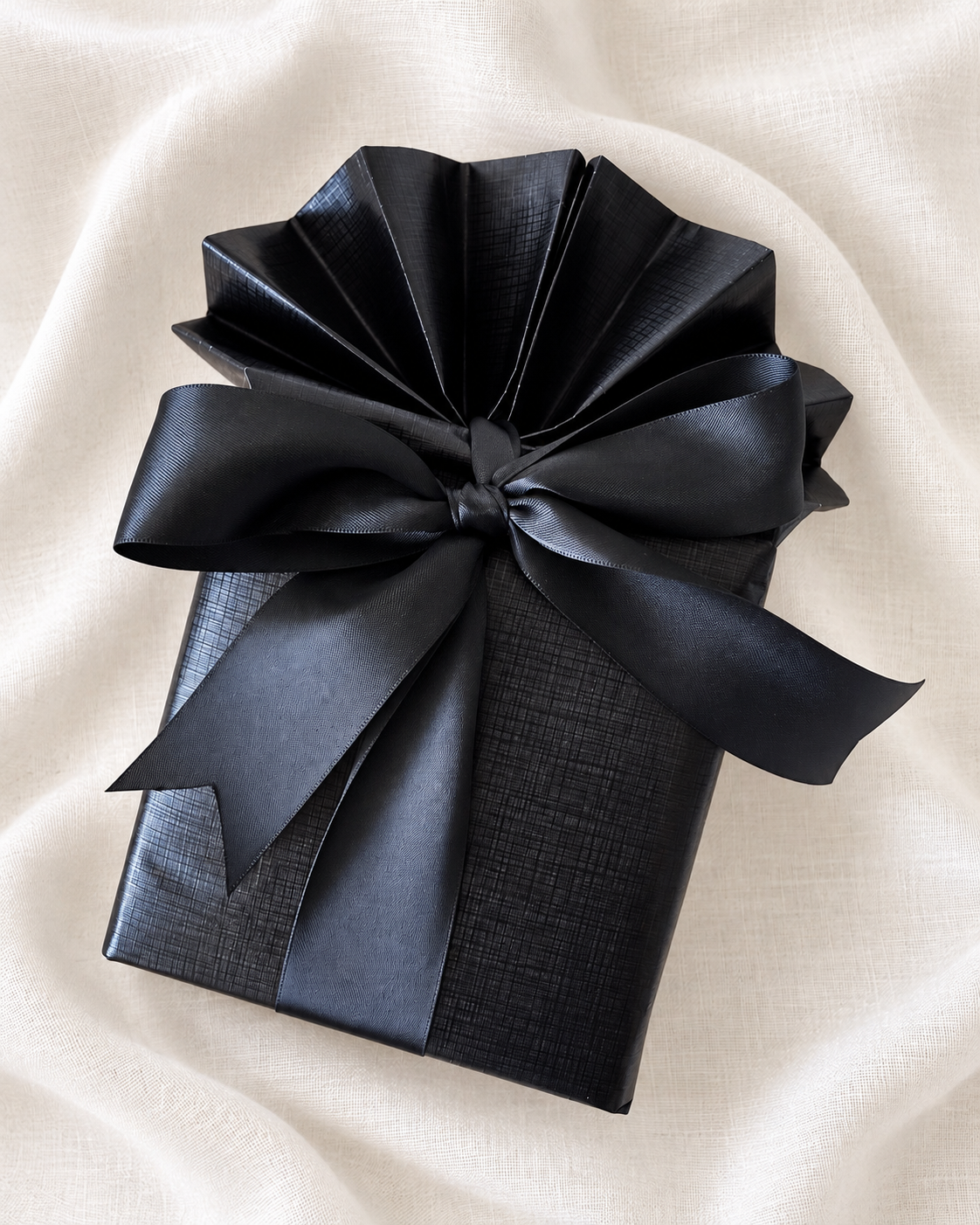 Black gift with a gathered paper top and black ribbon bow, viewed from above.