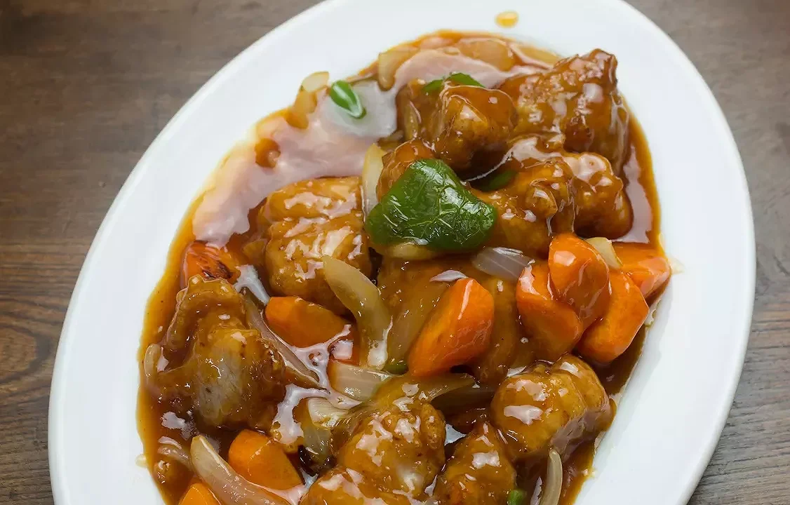 Plat de poulet à l'ananas avec légumes et sauce brune, servi sur une assiette blanche.