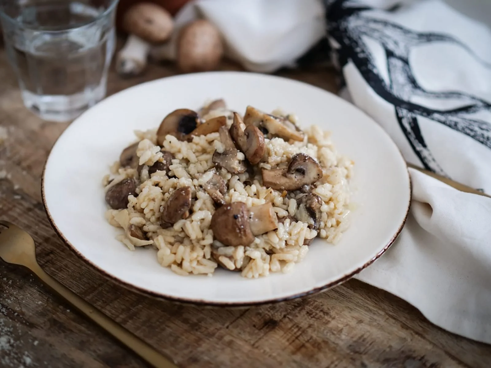 Un plat de risotto aux champignons dans une assiette blanche sur une table en bois.