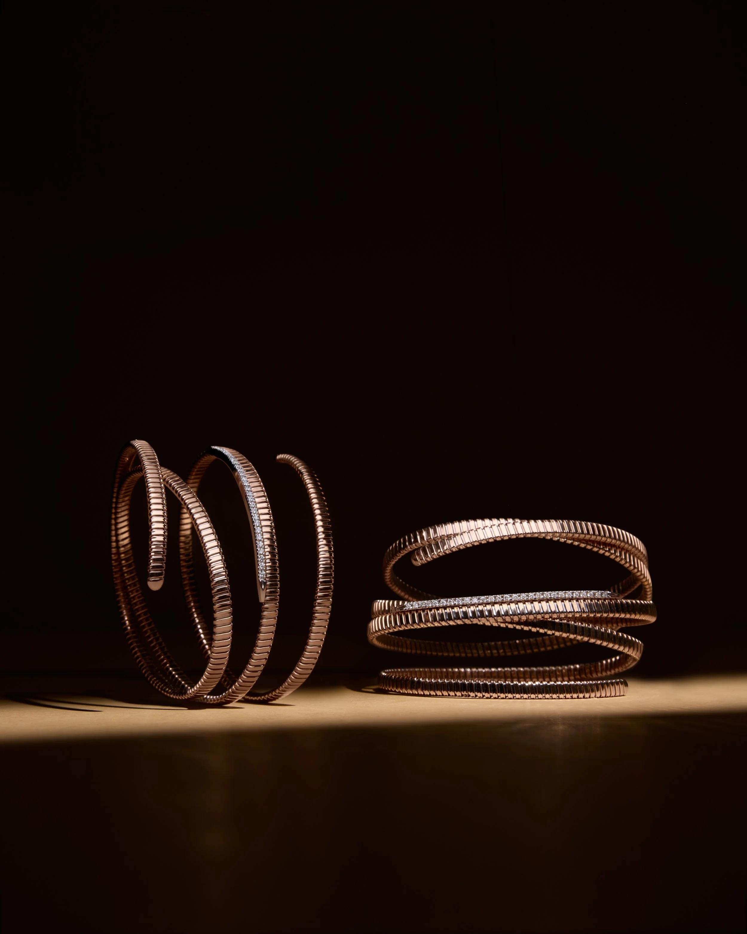 Several gold and silver bangles arranged on a surface with a dark background. K di Kuore jewelry.