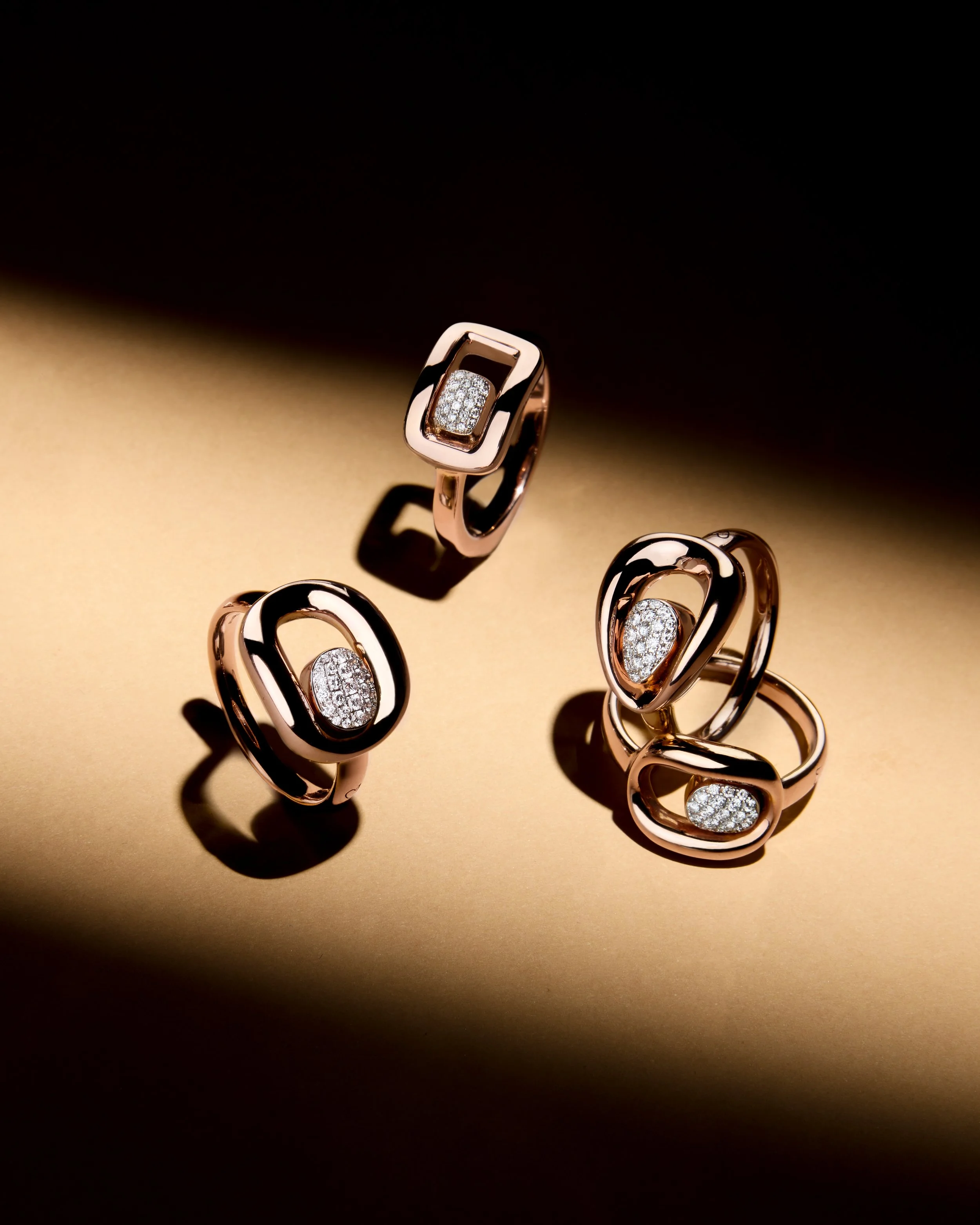 Set of elegant rose gold jewelry rings with embedded diamonds, displayed on a golden surface with shadow effects. K di Kuore jewelry.