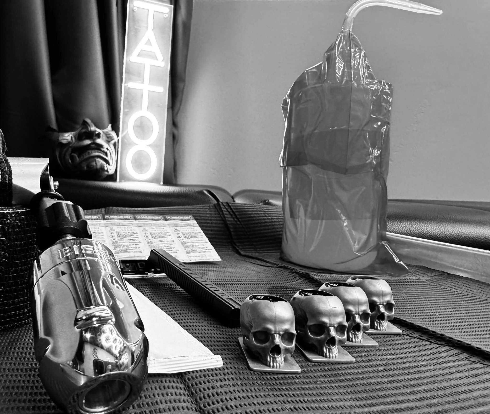 bishop tattoo machine with a Neon sign that reads "tattoo" skull ink cups. cool vibe set up, great atmosphere. professional set up for tattoos.