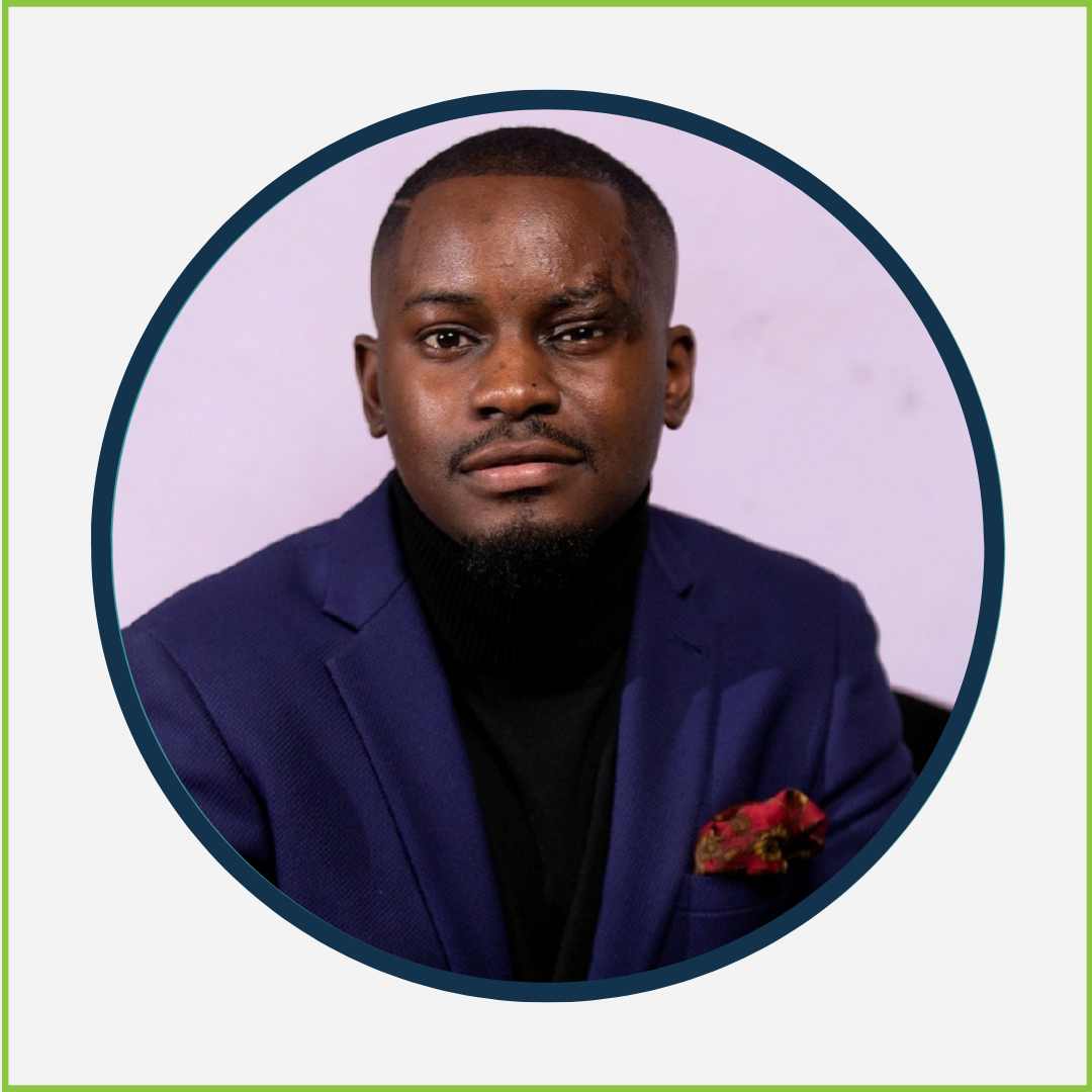 Portrait of a man with dark skin, wearing a dark blue blazer and a black turtleneck, with a red patterned pocket square, against a light-colored background.