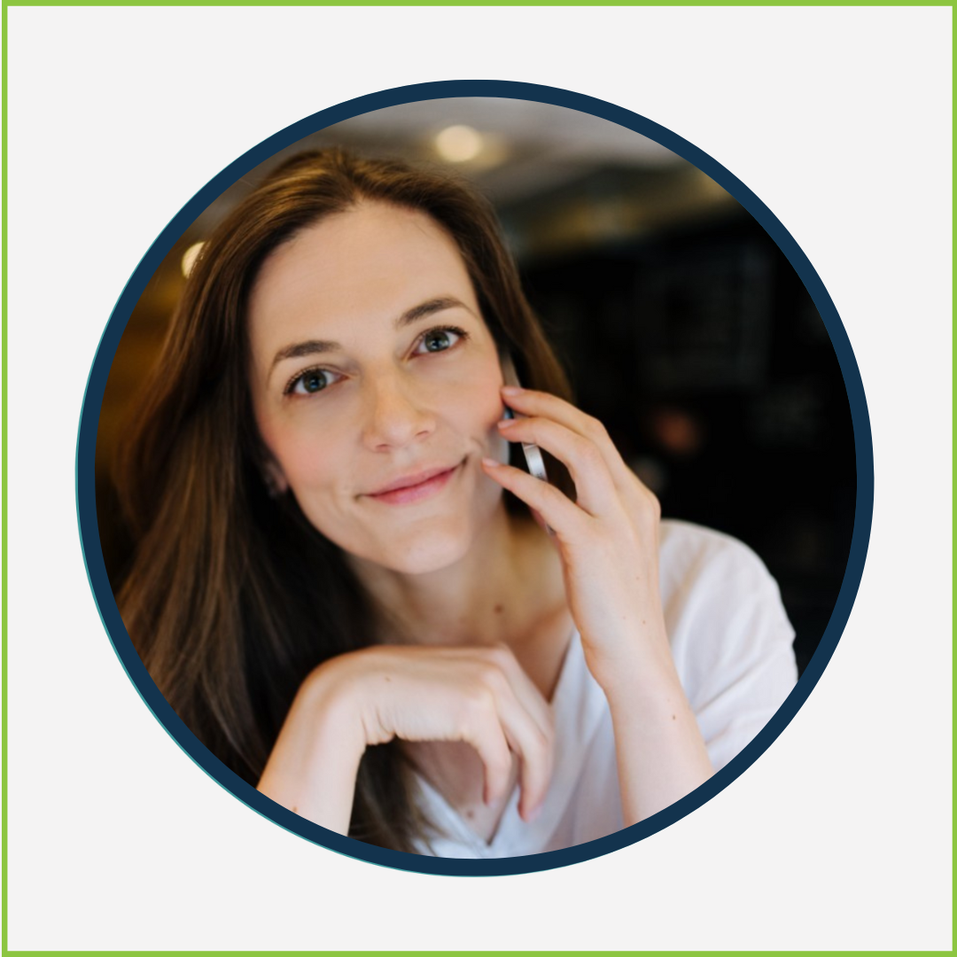 A woman with long brown hair and blue eyes, holding a phone to her ear and smiling softly.