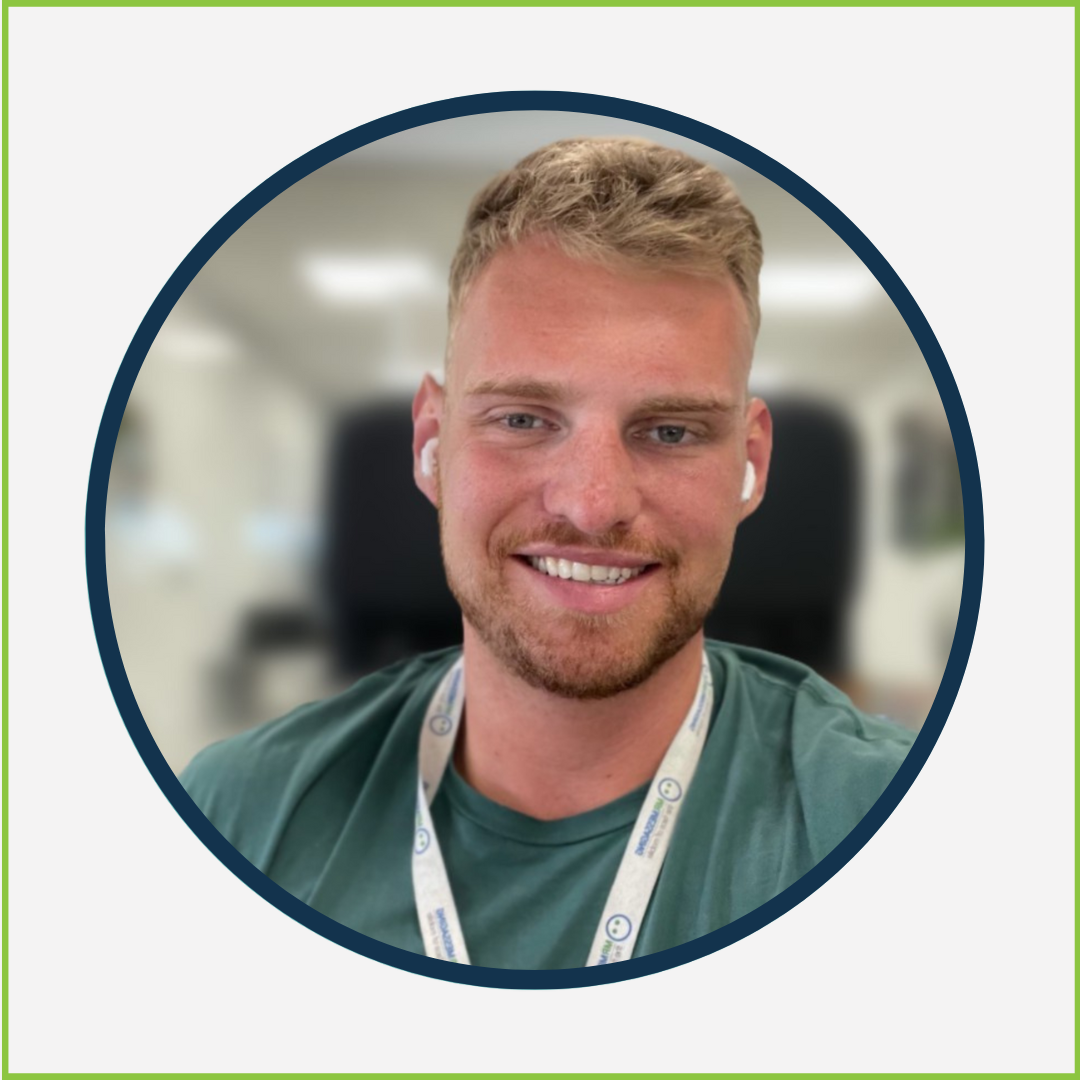 Happy young man with blond hair and a beard, using wireless earbuds and smiling, in a medical or office setting.