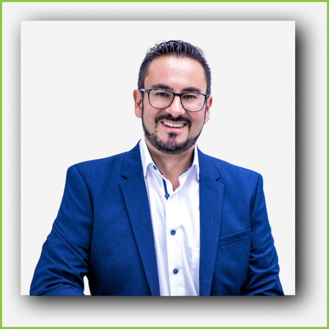 A man with glasses and a beard, wearing a blue suit and white shirt, smiling for the camera.
