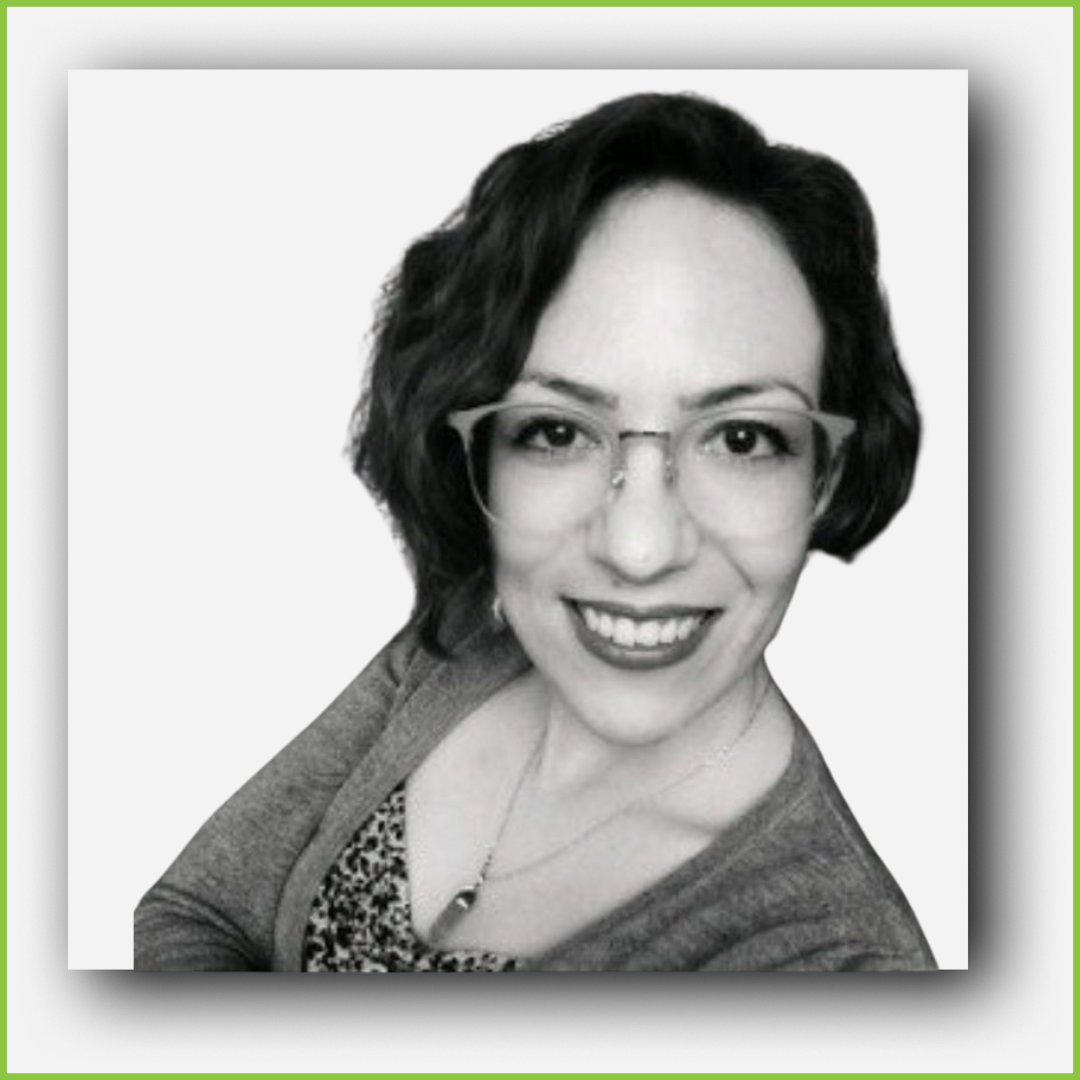 Black and white photo of a woman with short dark hair, glasses, and a smile, wearing a blazer and patterned top.