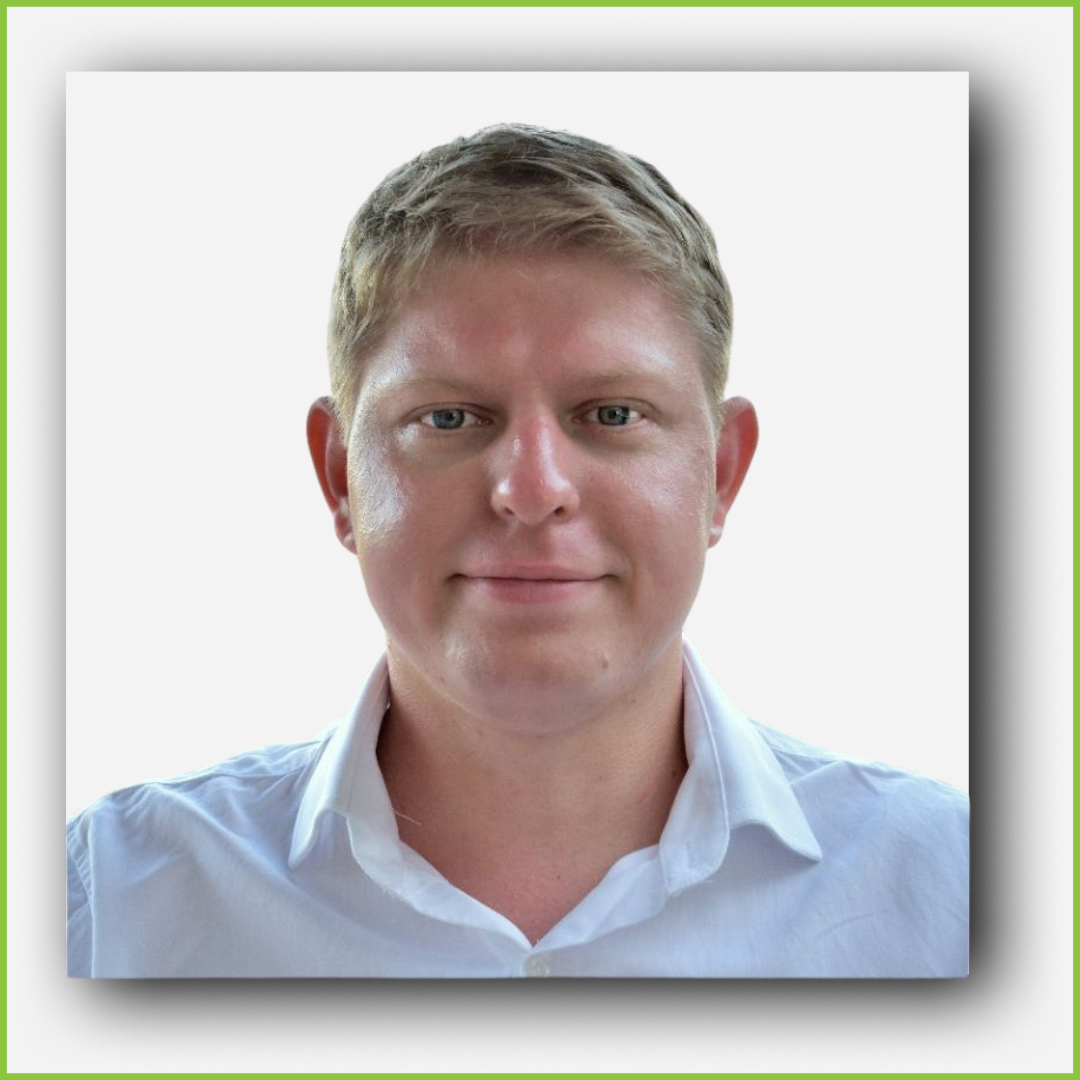 A young man with blonde hair and blue eyes wearing a white collared shirt, smiling against a plain white background.