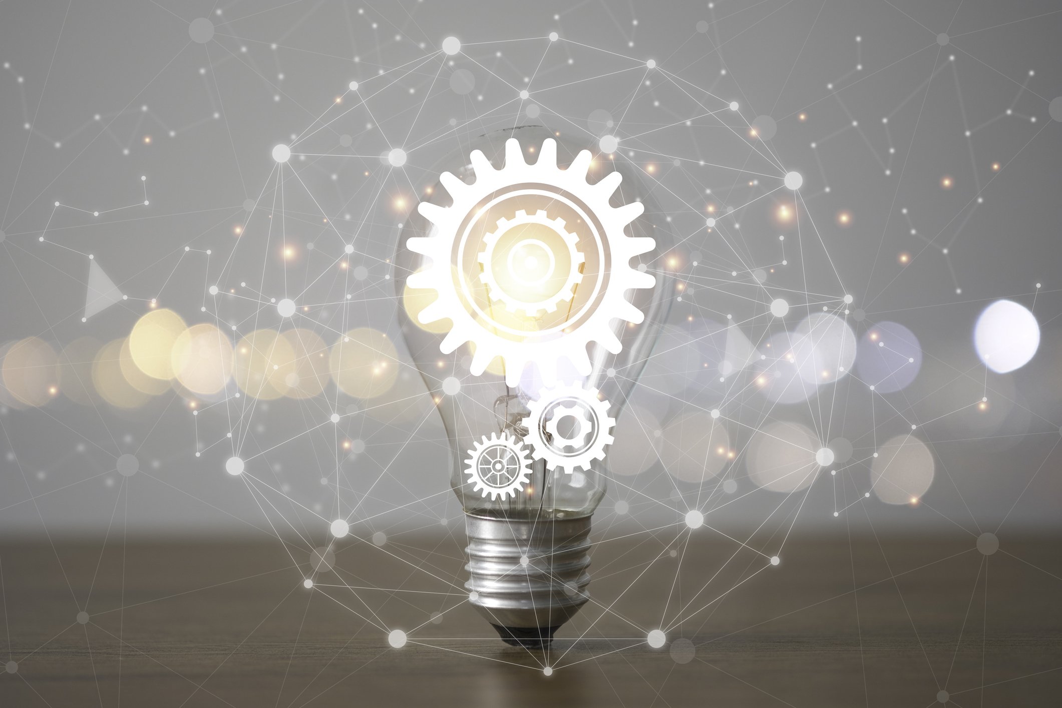 A light bulb with gear icons inside, overlaid with abstract network and gear illustrations, symbolizing innovation and technology.