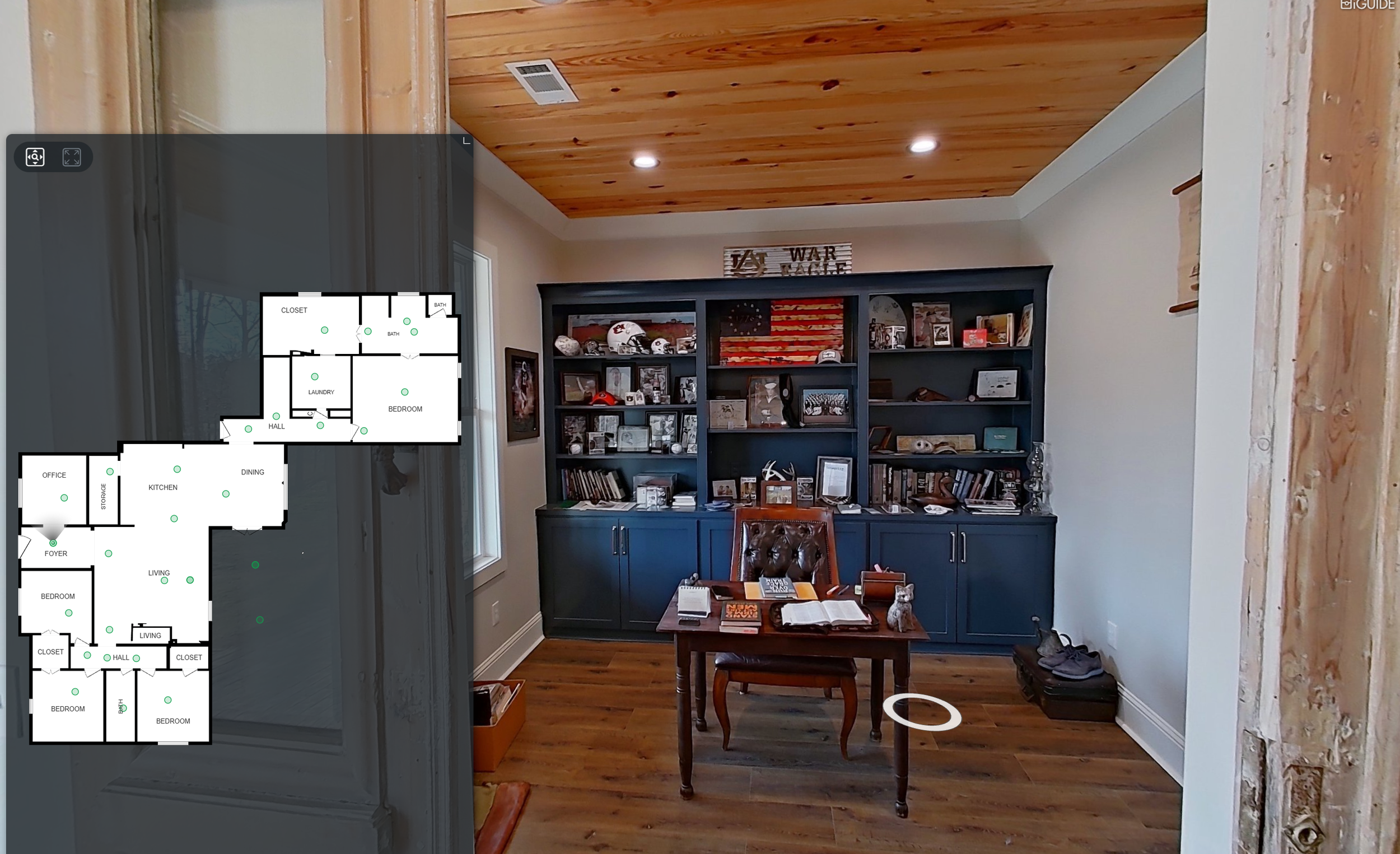 Living room with a blue bookshelf filled with books and sports memorabilia, a small wooden desk and leather chair, hardwood floor, and a window with light curtain. Floor plans overlay showing layouts of multiple rooms.
