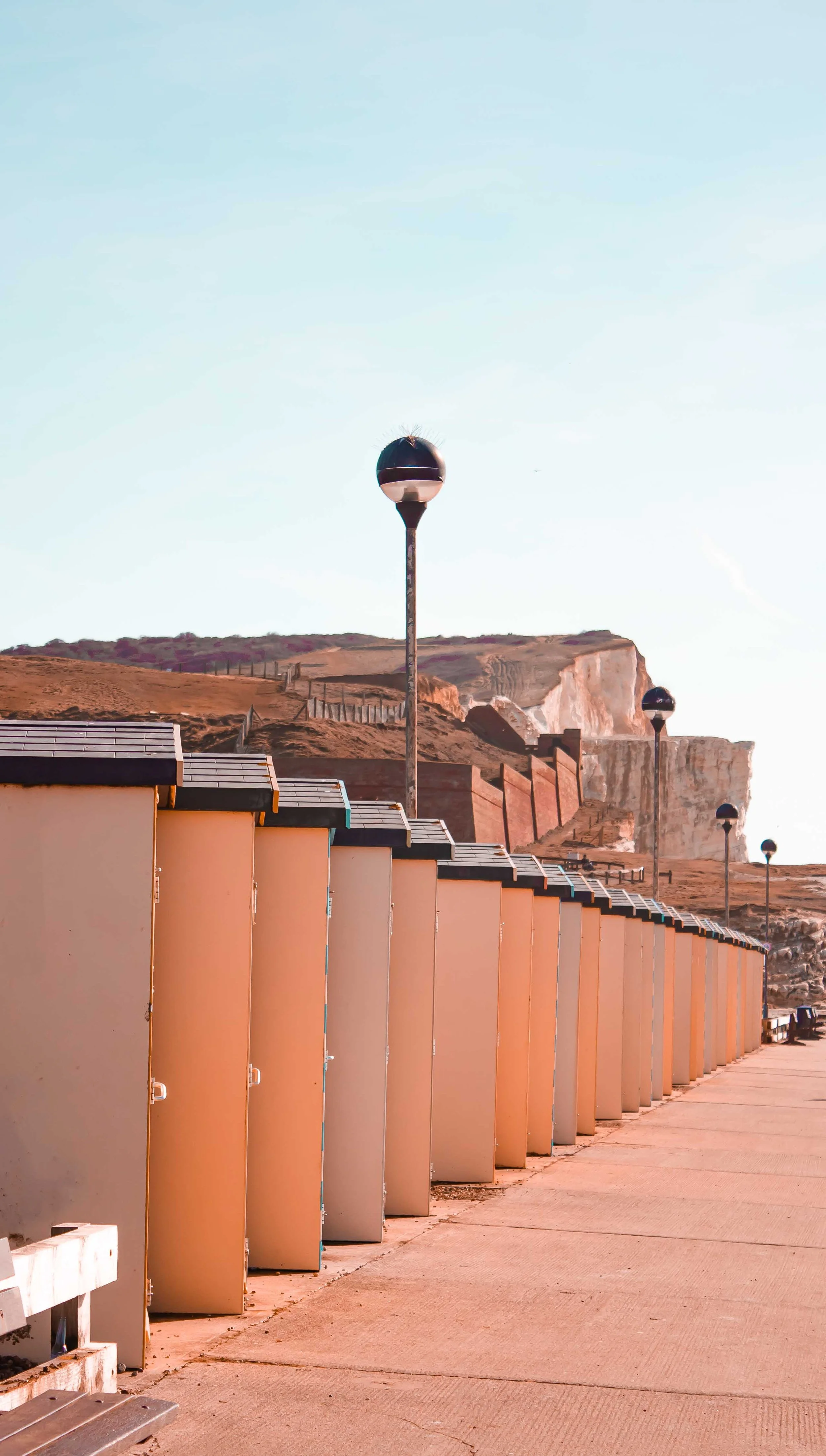 Beachside row of changing cabins with street lamps against cliffs in the background on a clear day.