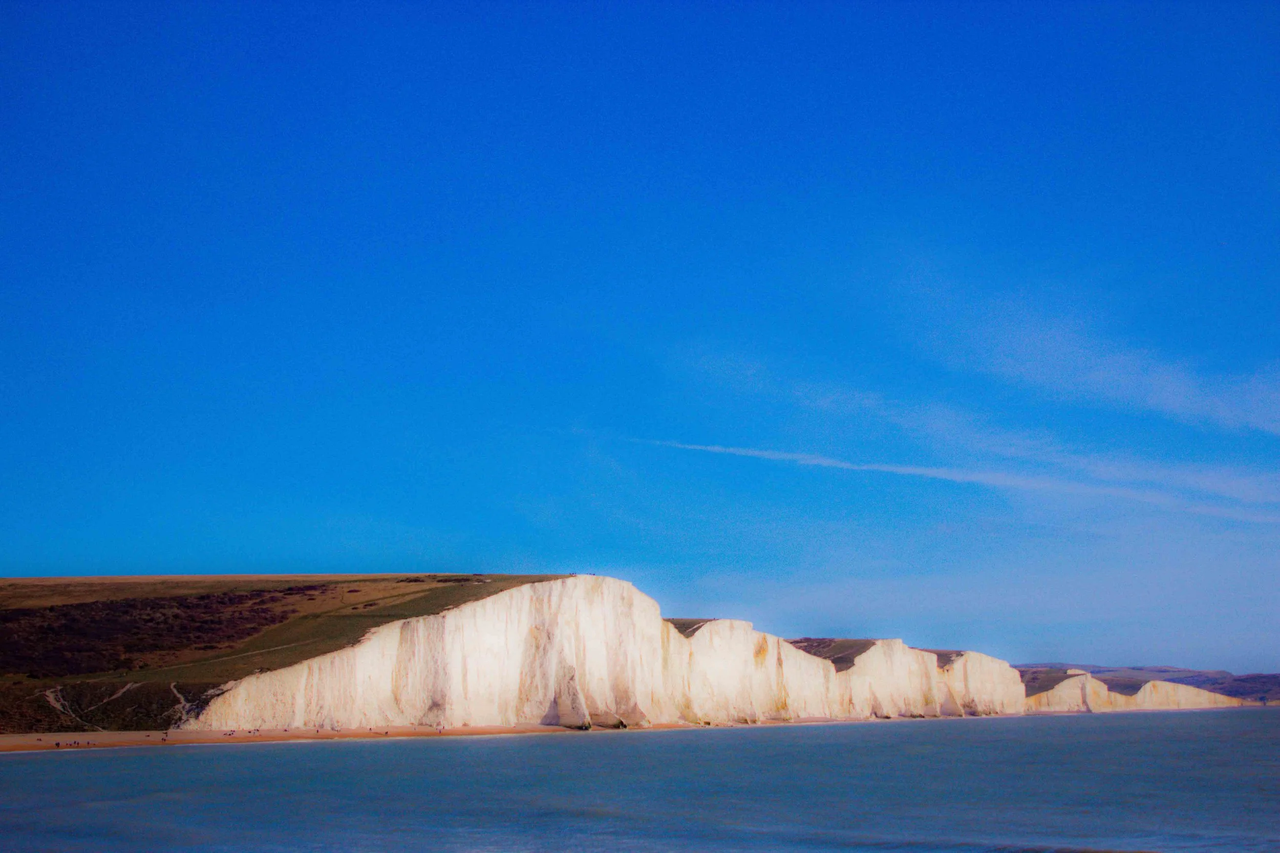 Cliffs of Dover under a clear blue sky, overlooking blue water.