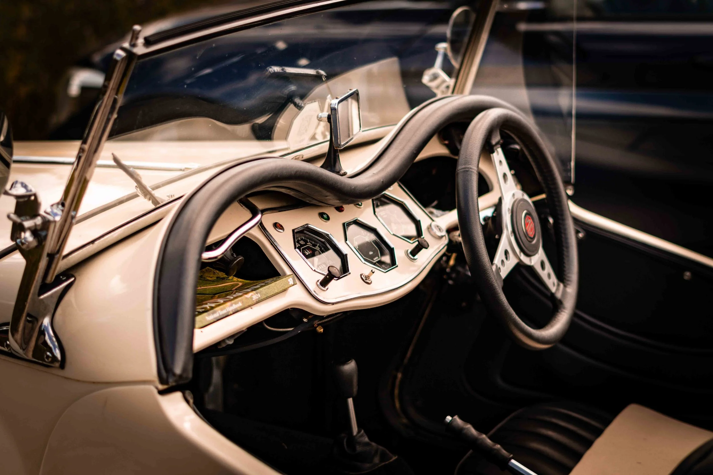 Close-up of the dashboard and steering wheel of a vintage race car, featuring classic gauges, switches, and a wooden steering wheel.