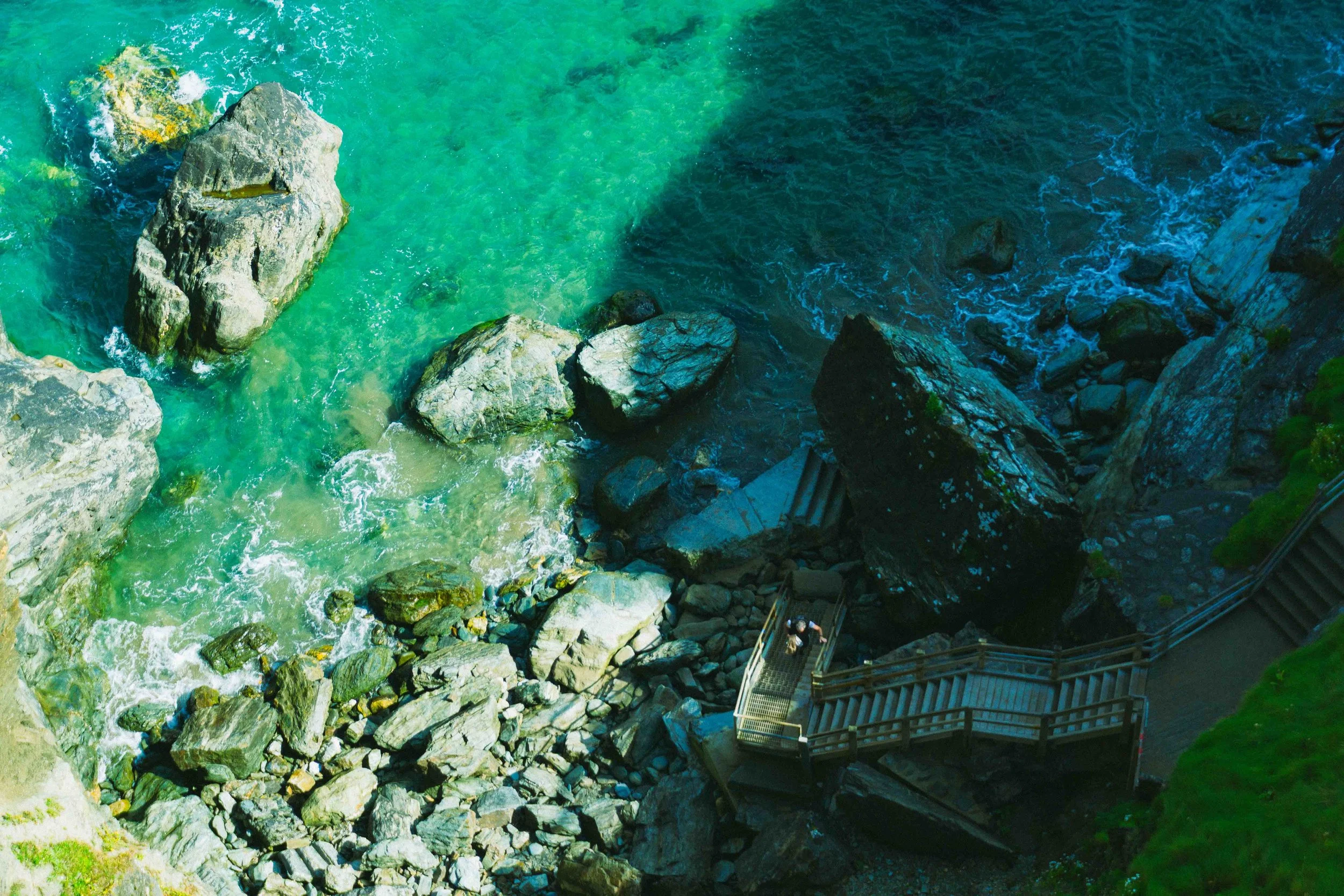 Bird's eye view of a rocky shoreline with greenish-blue water and a staircase leading down to the rocks.