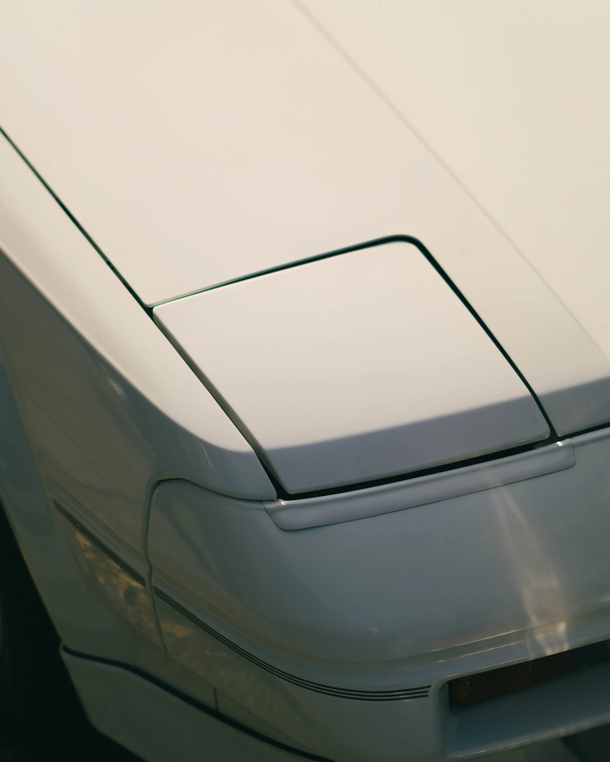 Close-up of a classic white sports car hood and front bumper, focusing on the clean lines and minimalistic design.