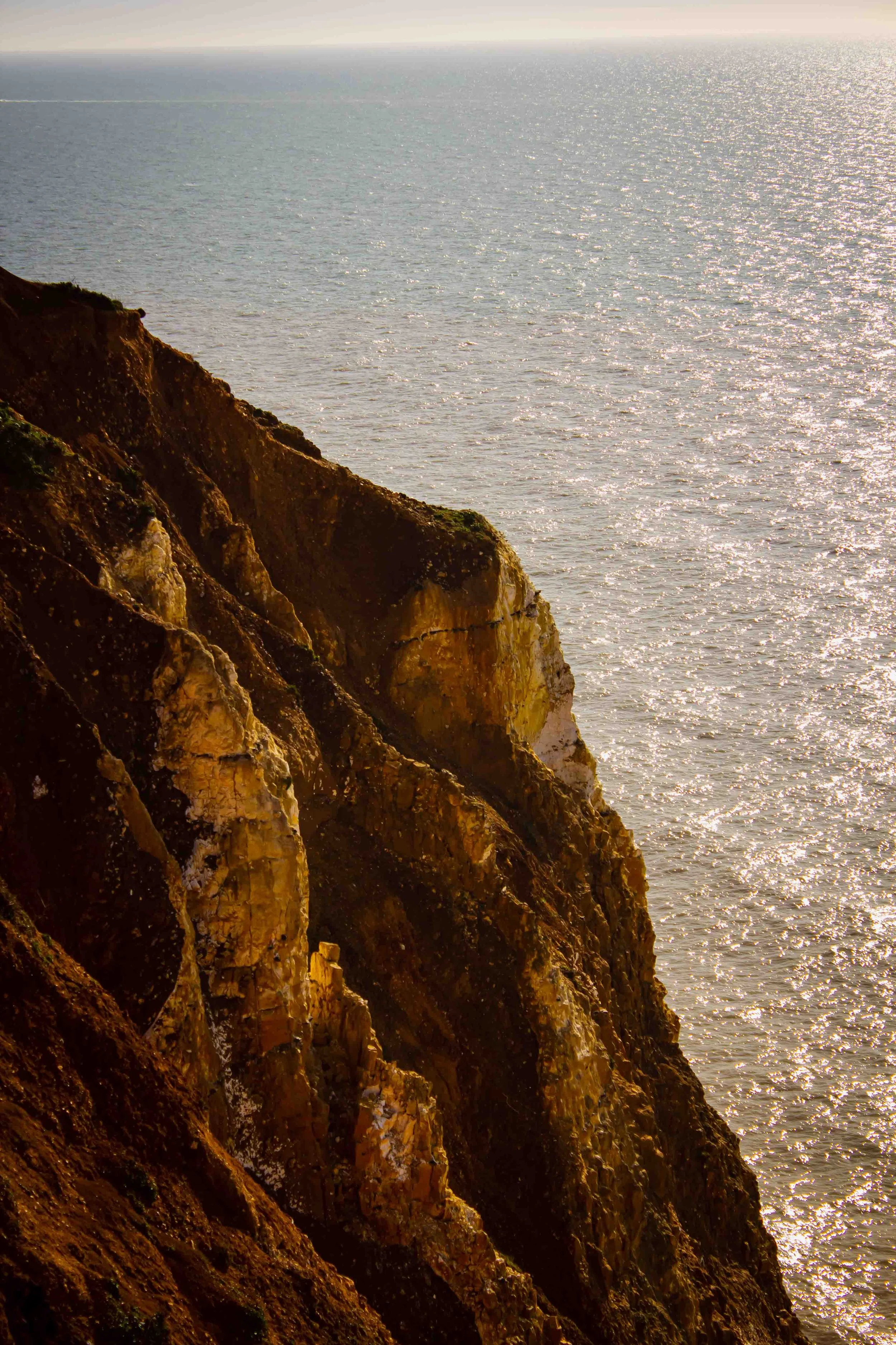 Cliffside overlooking the ocean, with sunlight reflecting off the water.