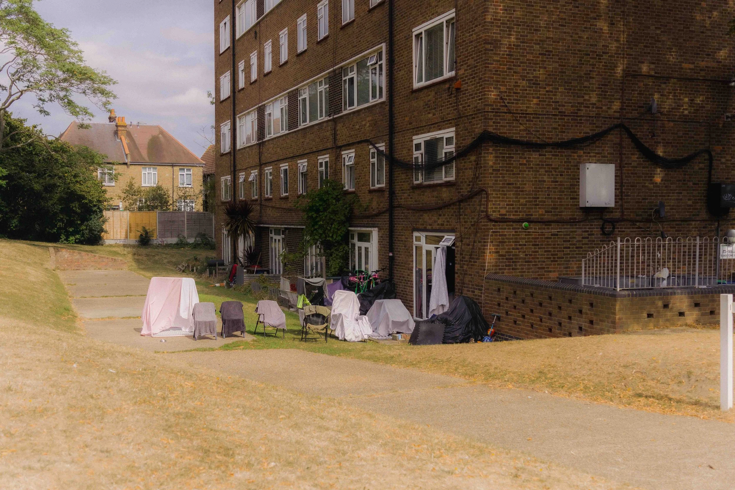 Clothes and household items covered with cloths and tarps outside an apartment building on a grassy area