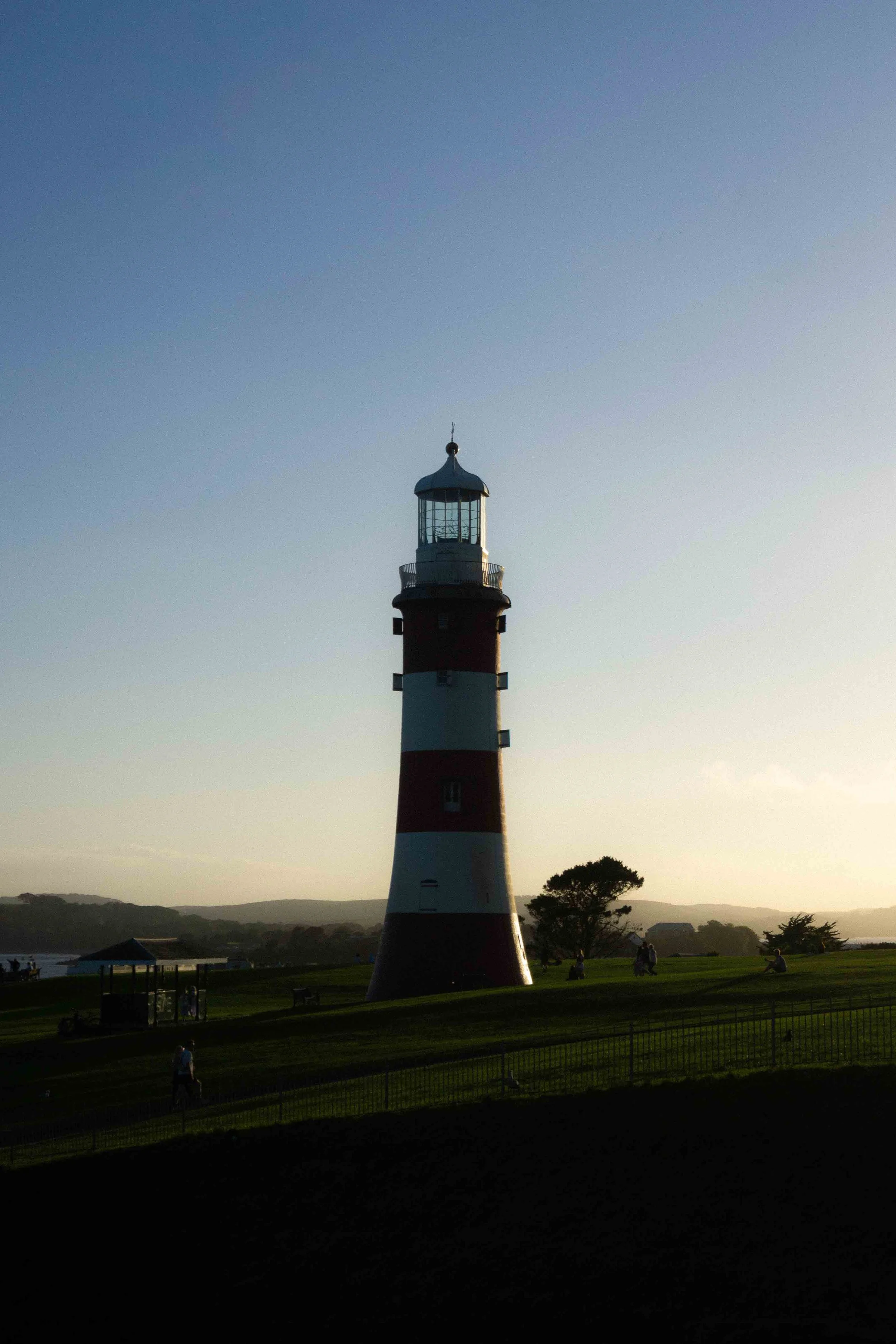 Lighthouse with red and white stripes on a grassy area during sunset.