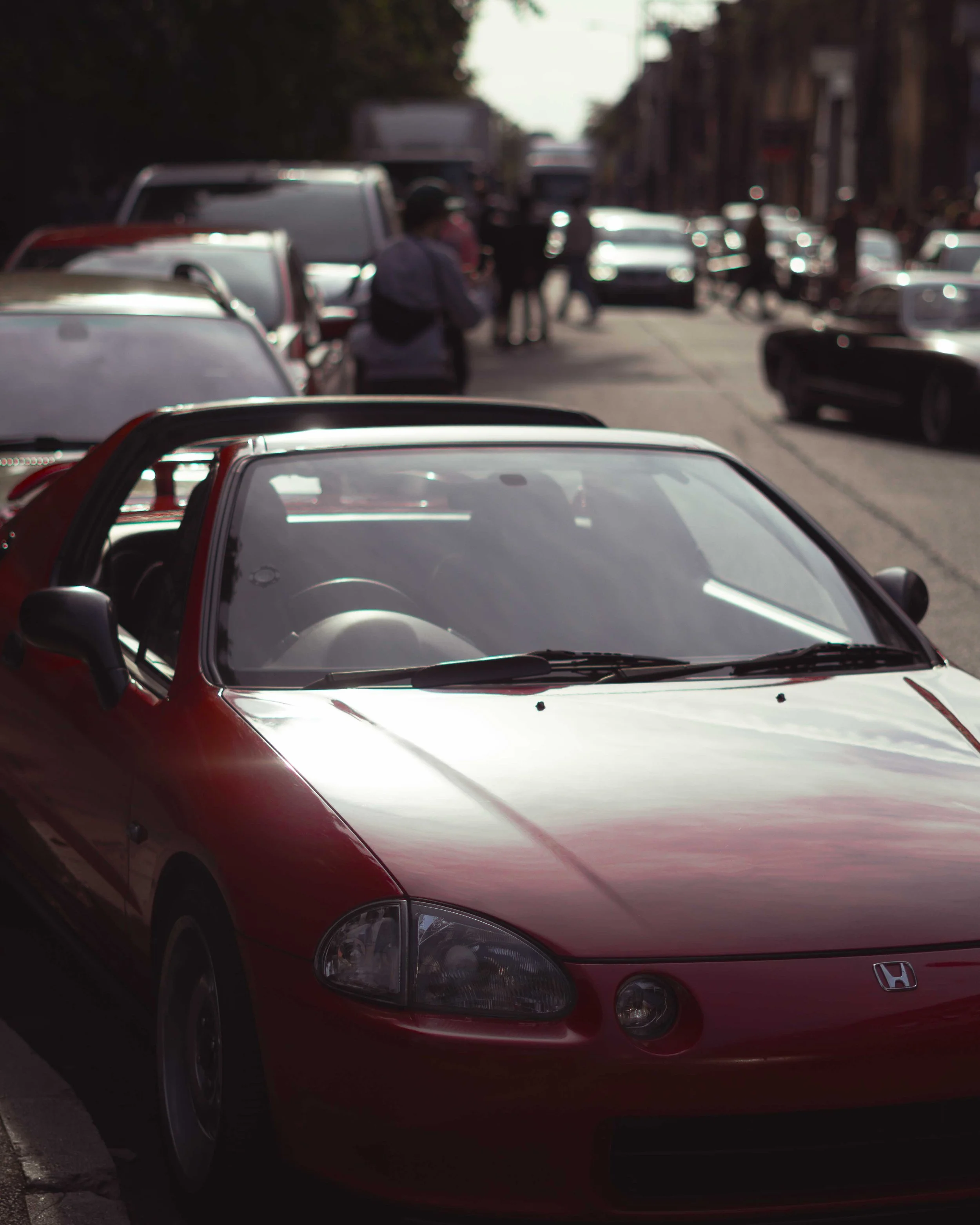 A red Honda convertible parked on a busy city street with pedestrians walking in the background.