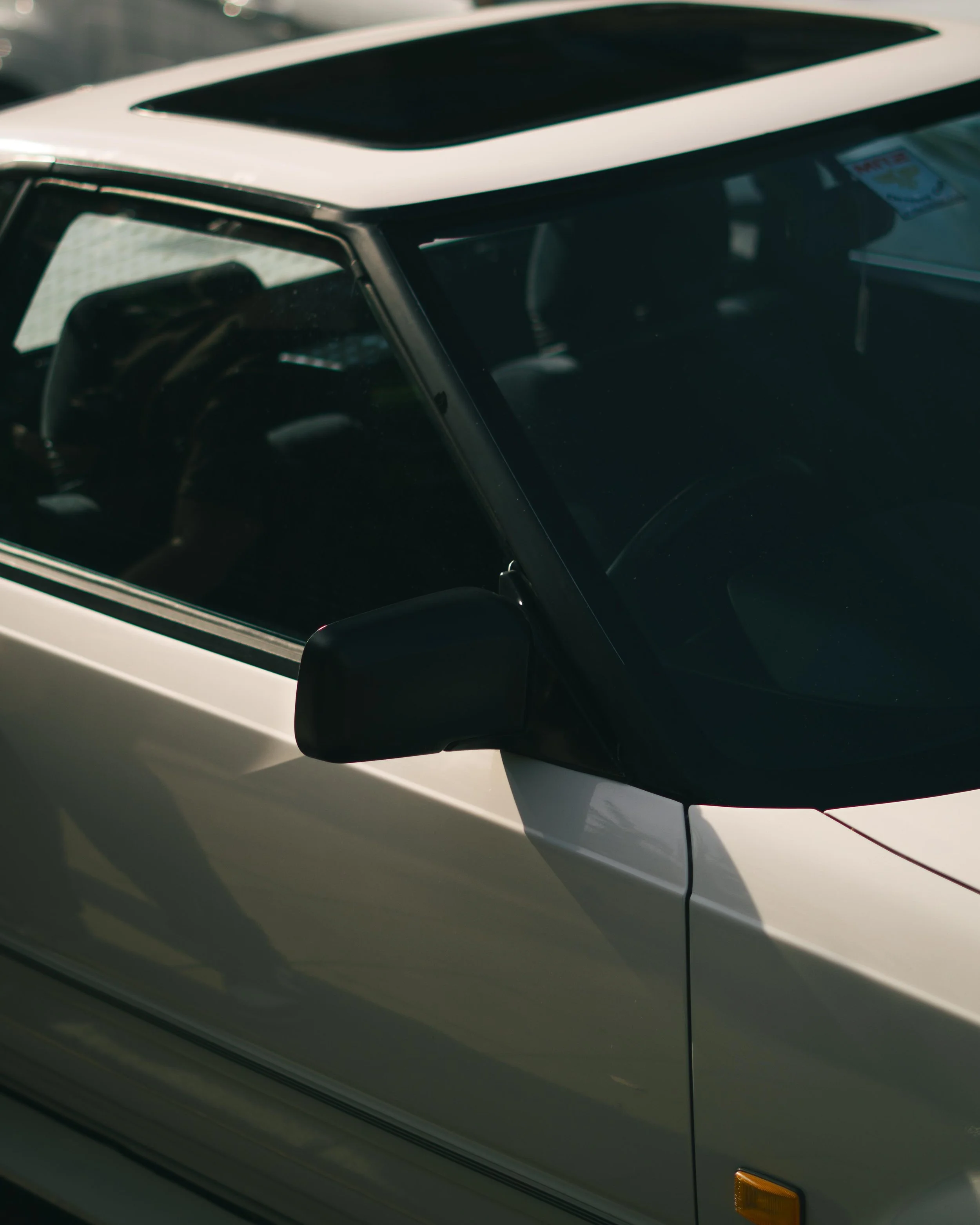 Close-up of the front side of a white vintage car, focusing on the windshield, side mirror, and part of the door.