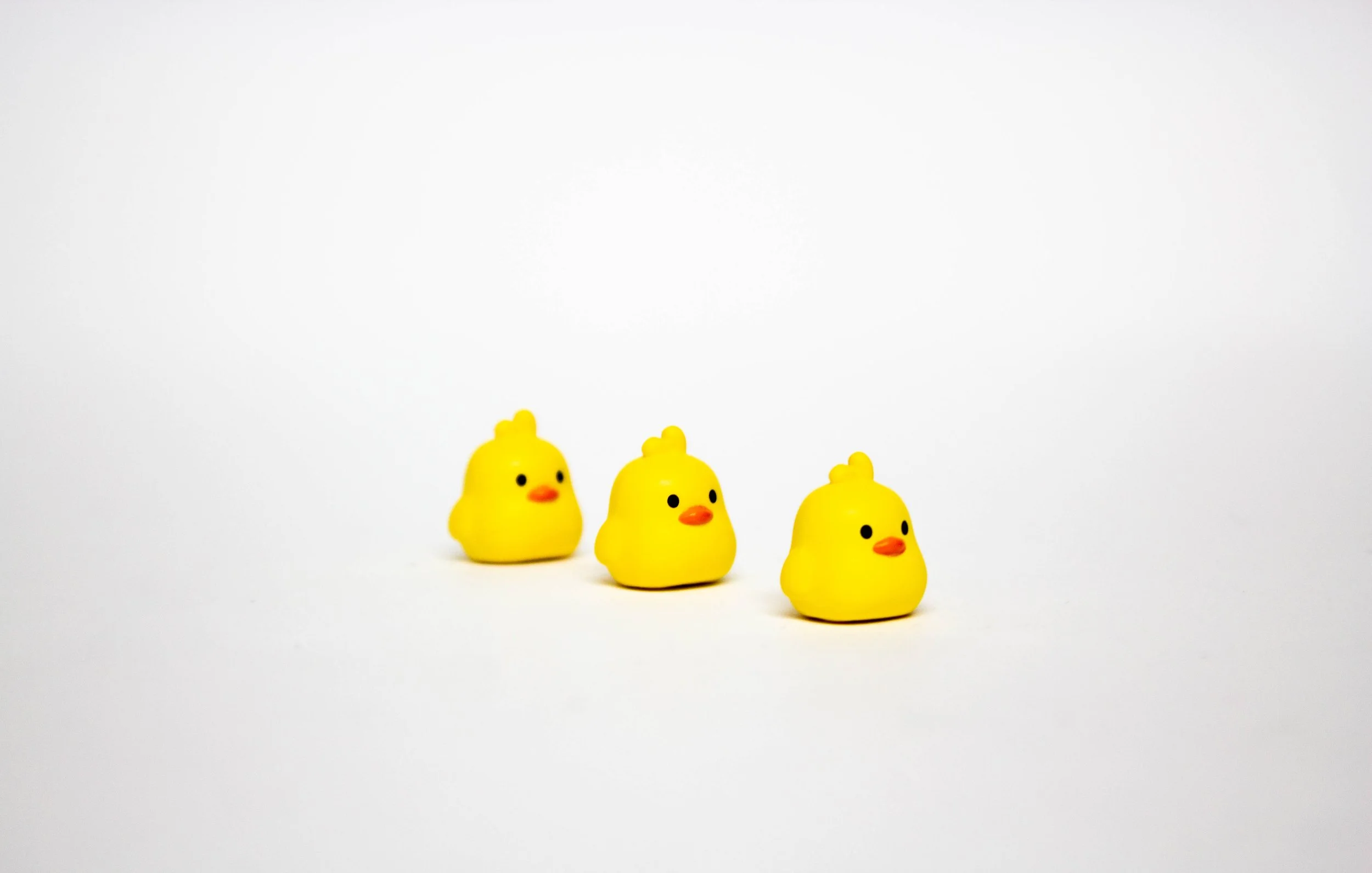Three small yellow rubber duck toys arranged in a row on a plain white surface with a white background.