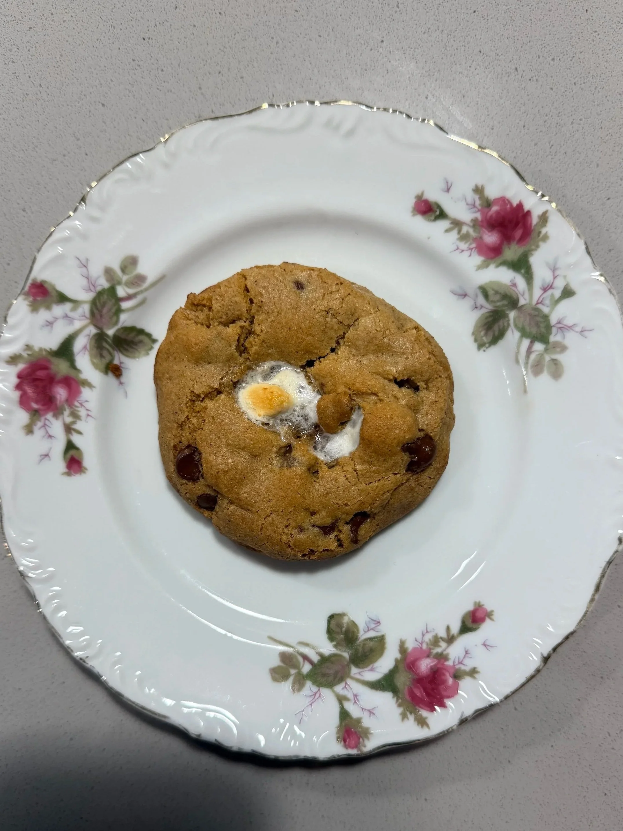 A cookie with half-melted marshmallow and chocolate chips on a floral patterned plate.