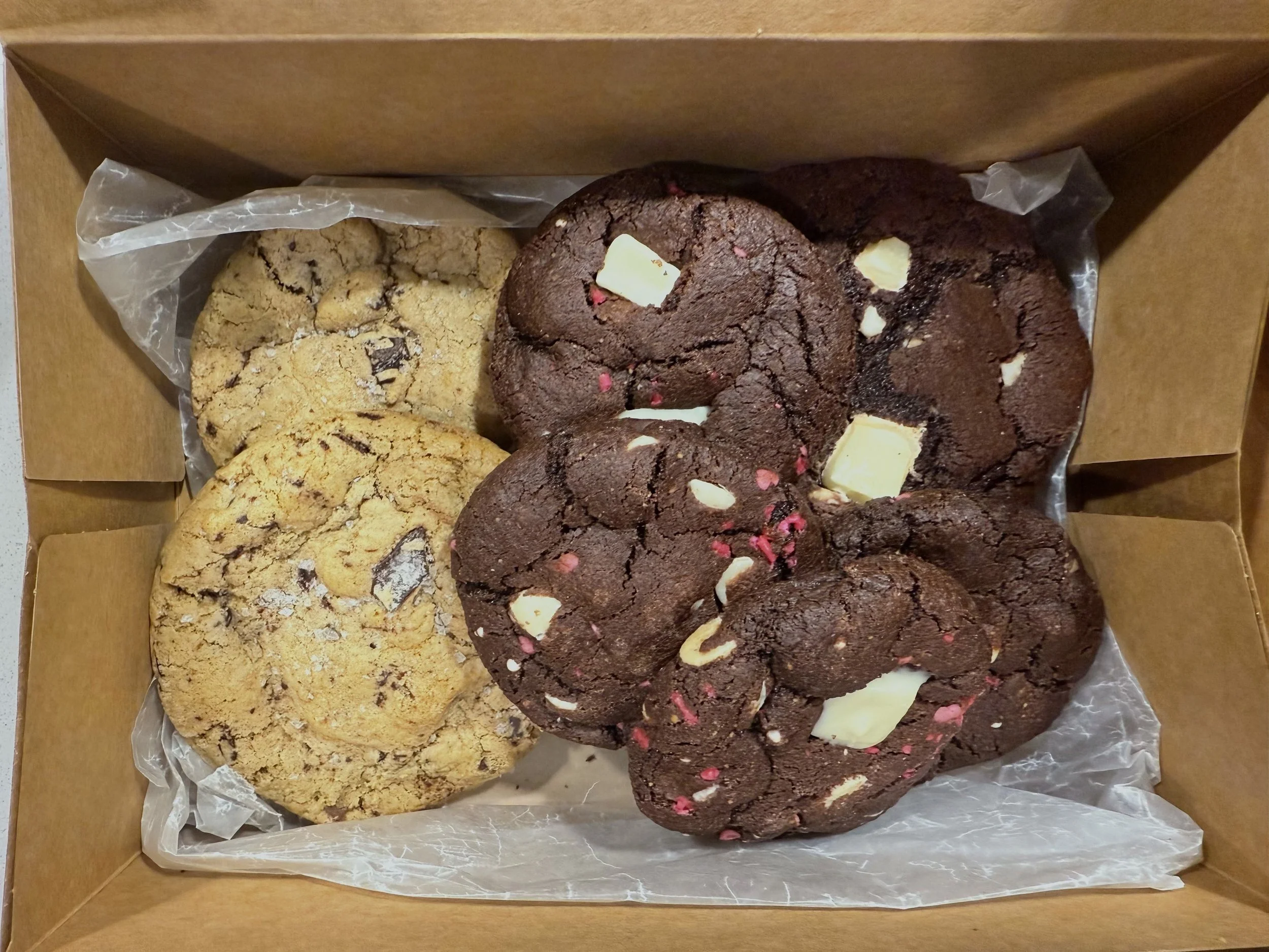 A box containing two types of cookies: chocolate chip cookies with white and pink chocolate chunks on the right, and oatmeal cookies with chocolate chips on the left.
