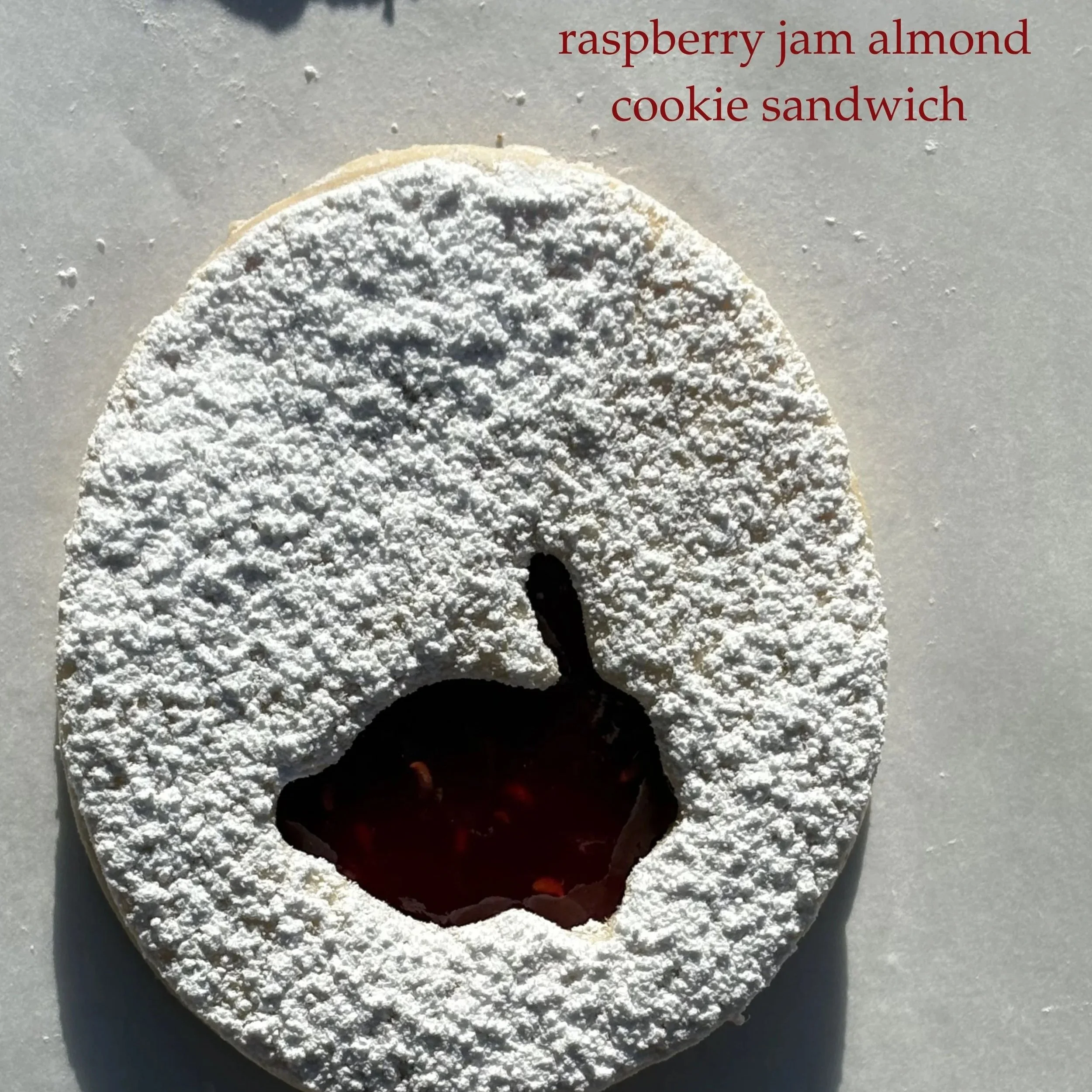A round cookie with powdered sugar, cut out in the shape of an apple's profile, with raspberry jam filling inside.