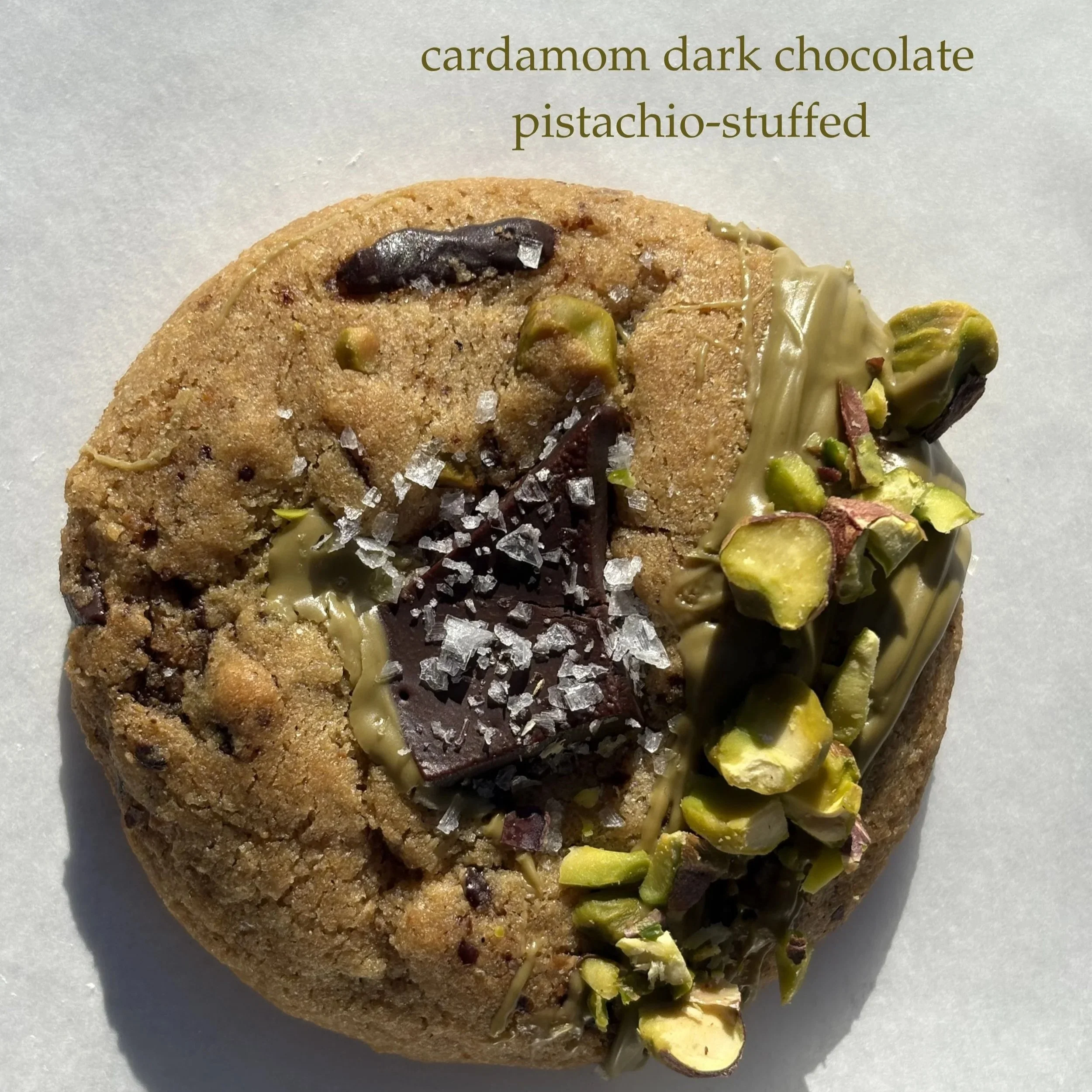 Close-up of a cardamom dark chocolate pistachio-stuffed cookie topped with sea salt and chopped pistachios.
