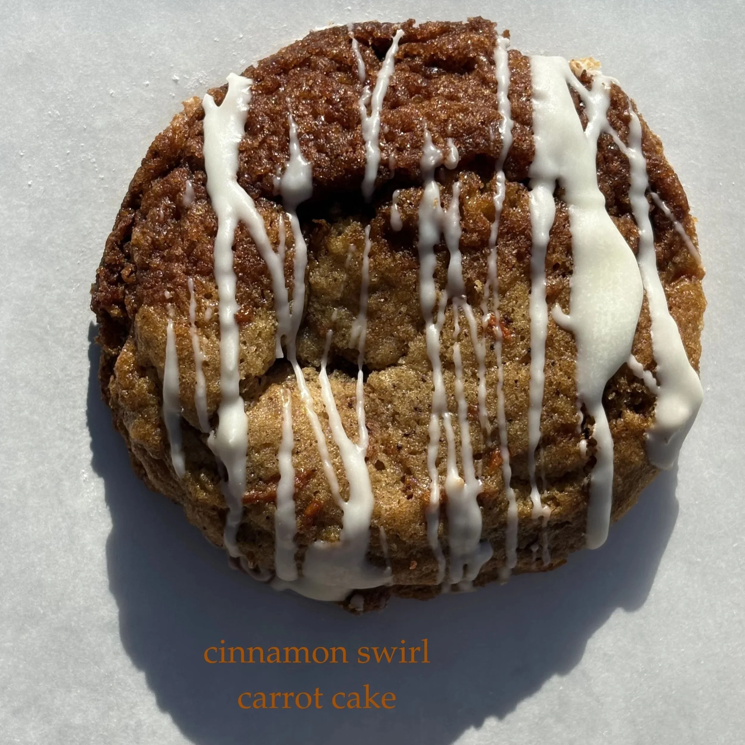 A cinnamon swirl carrot cake decorated with white icing drizzles on top.