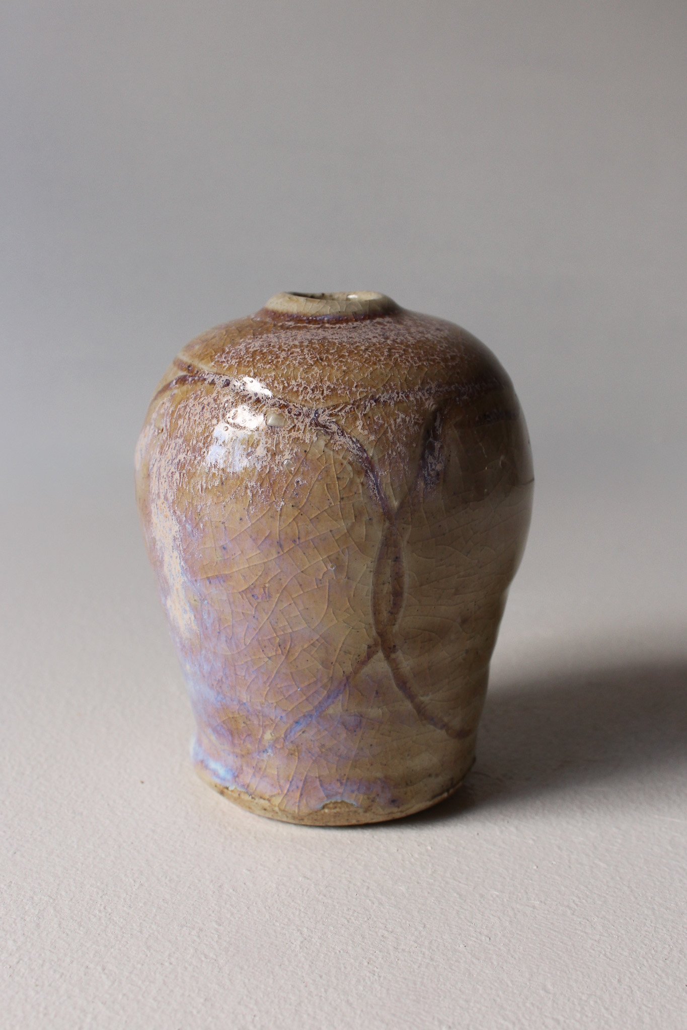 A ceramic vase with a crackled glaze finish in earthy tones of beige, brown, and purple, set against a neutral background.