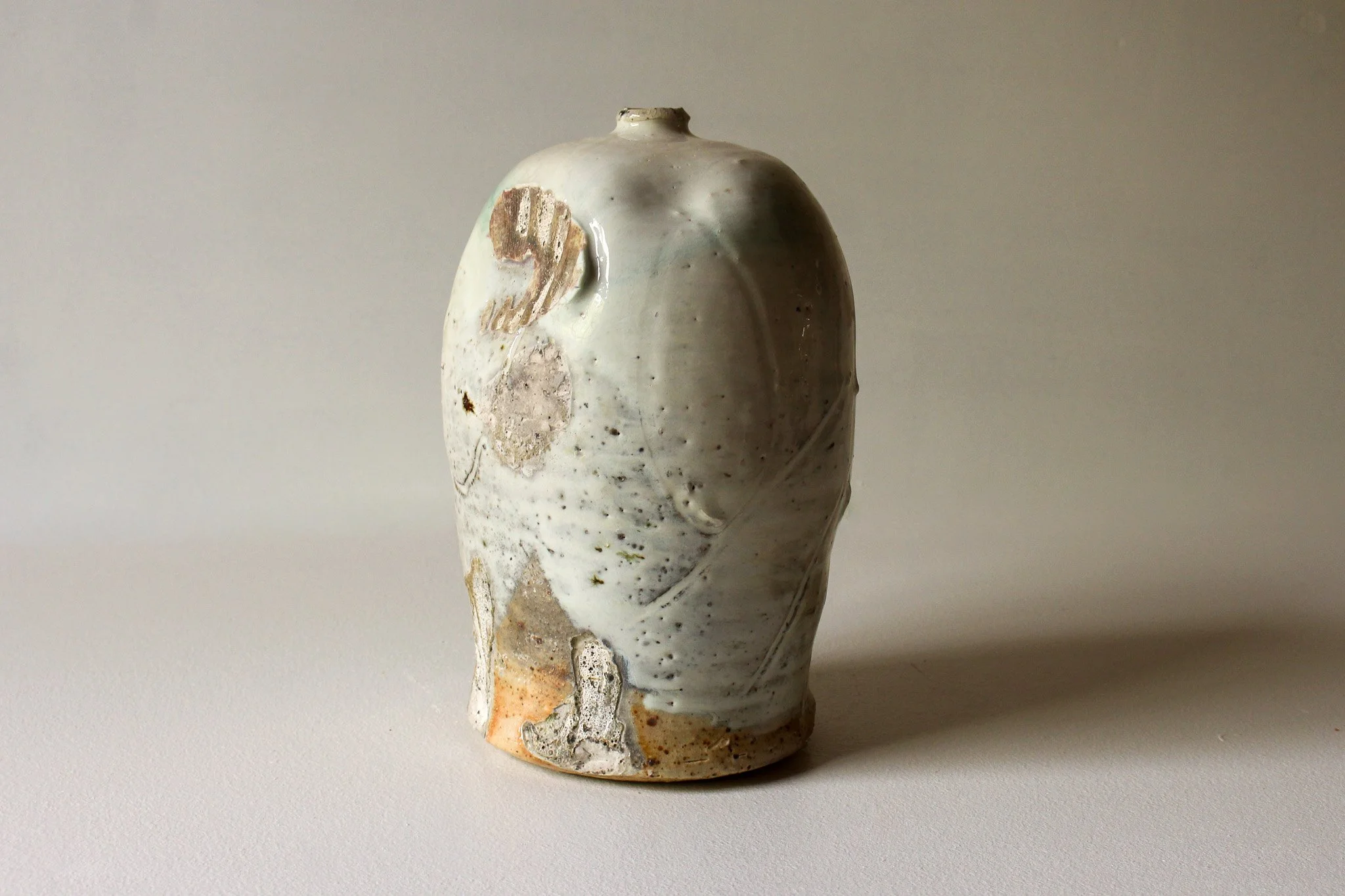 Ceramic vase with a rounded top, decorated with earthy tones, patterns, and textured surface, placed on a white background.