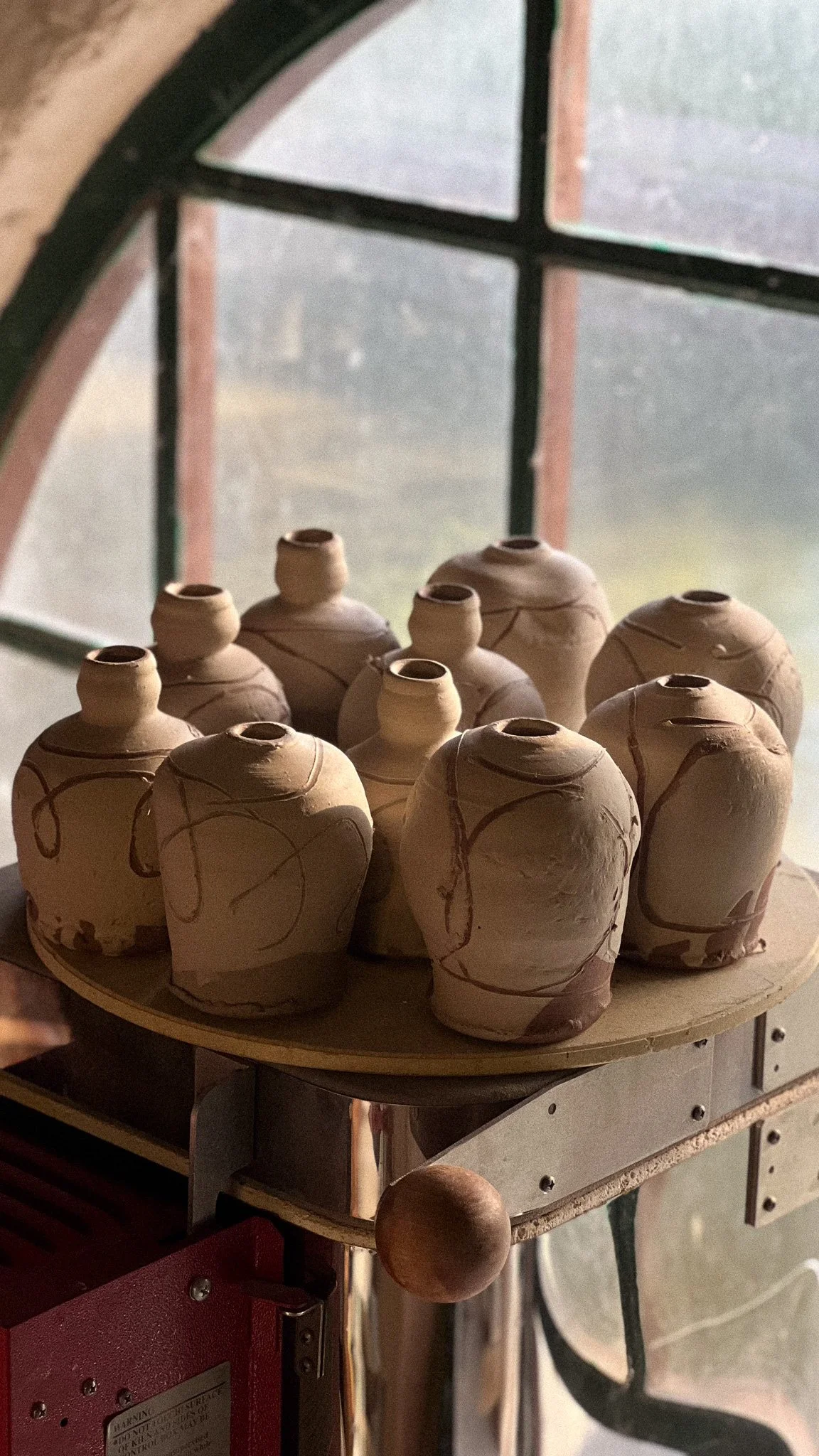 A collection of small, unglazed clay pots with decorative lines and patterns, arranged on a round tray.