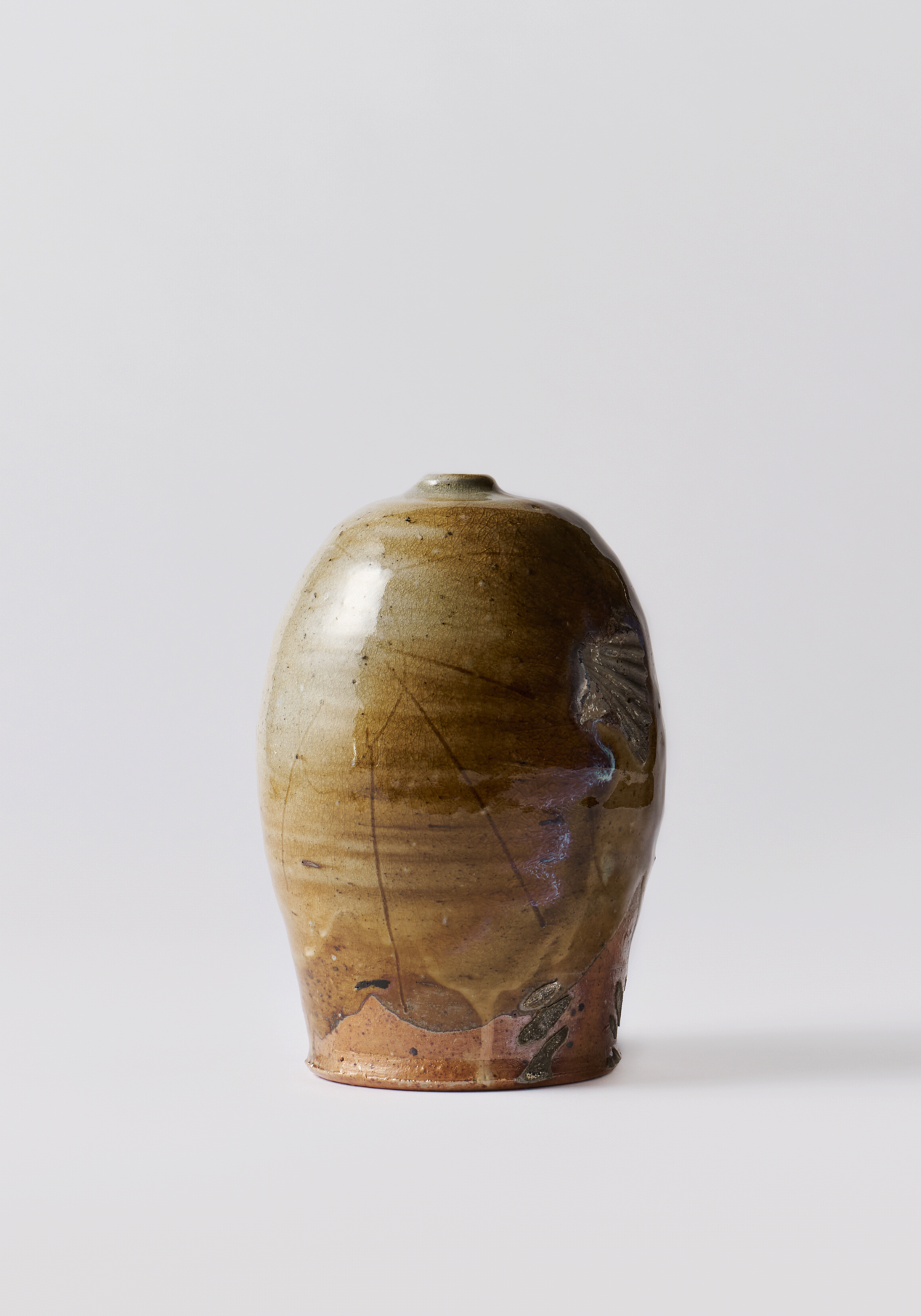 A ceramic vase with a rounded body, glazed in earthy tones of beige, brown, and hints of black, featuring visible cracks and textured surface detailing.