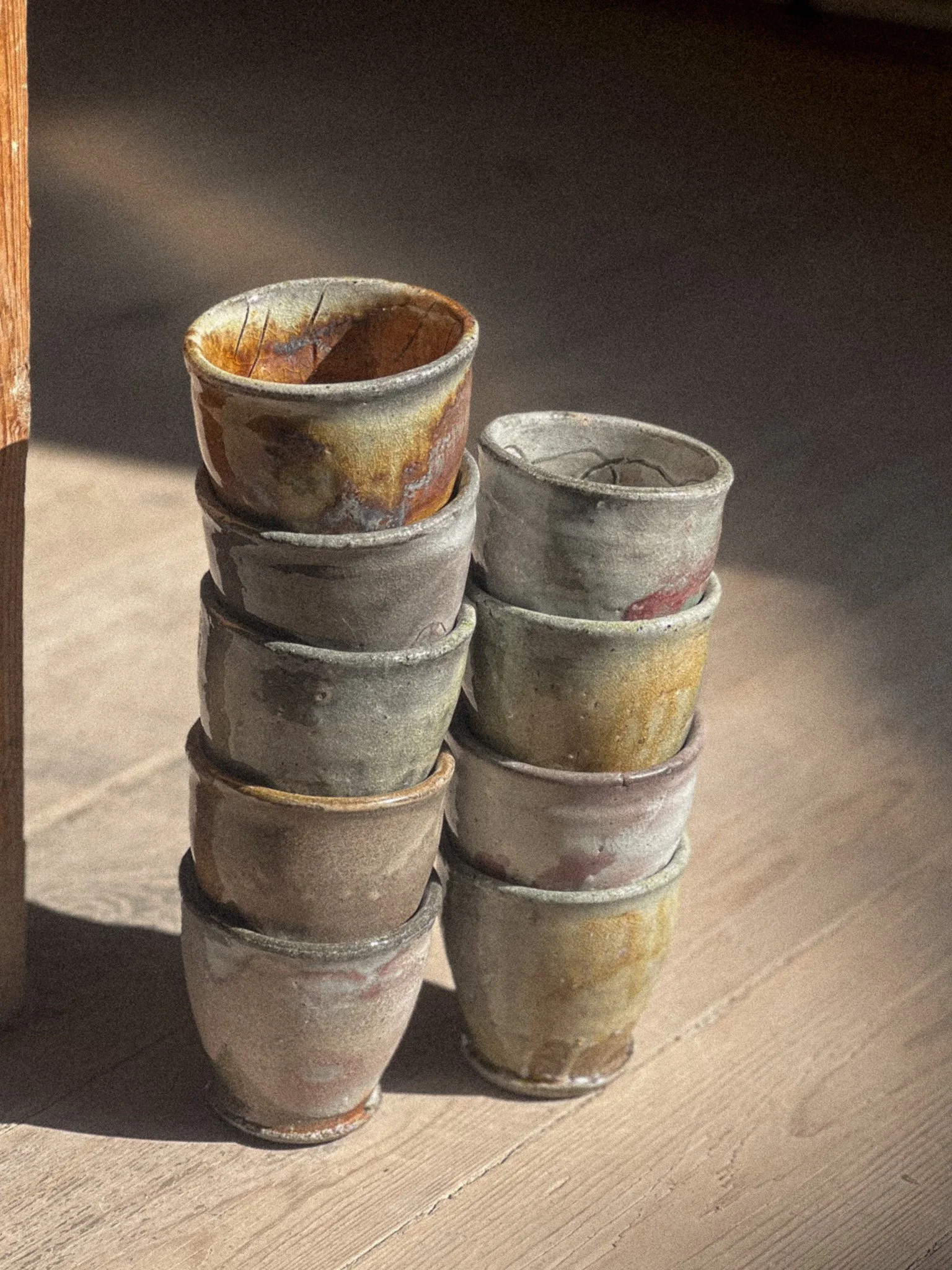 Staggered stacks of small ceramic cups with a rustic appearance on a wooden surface.