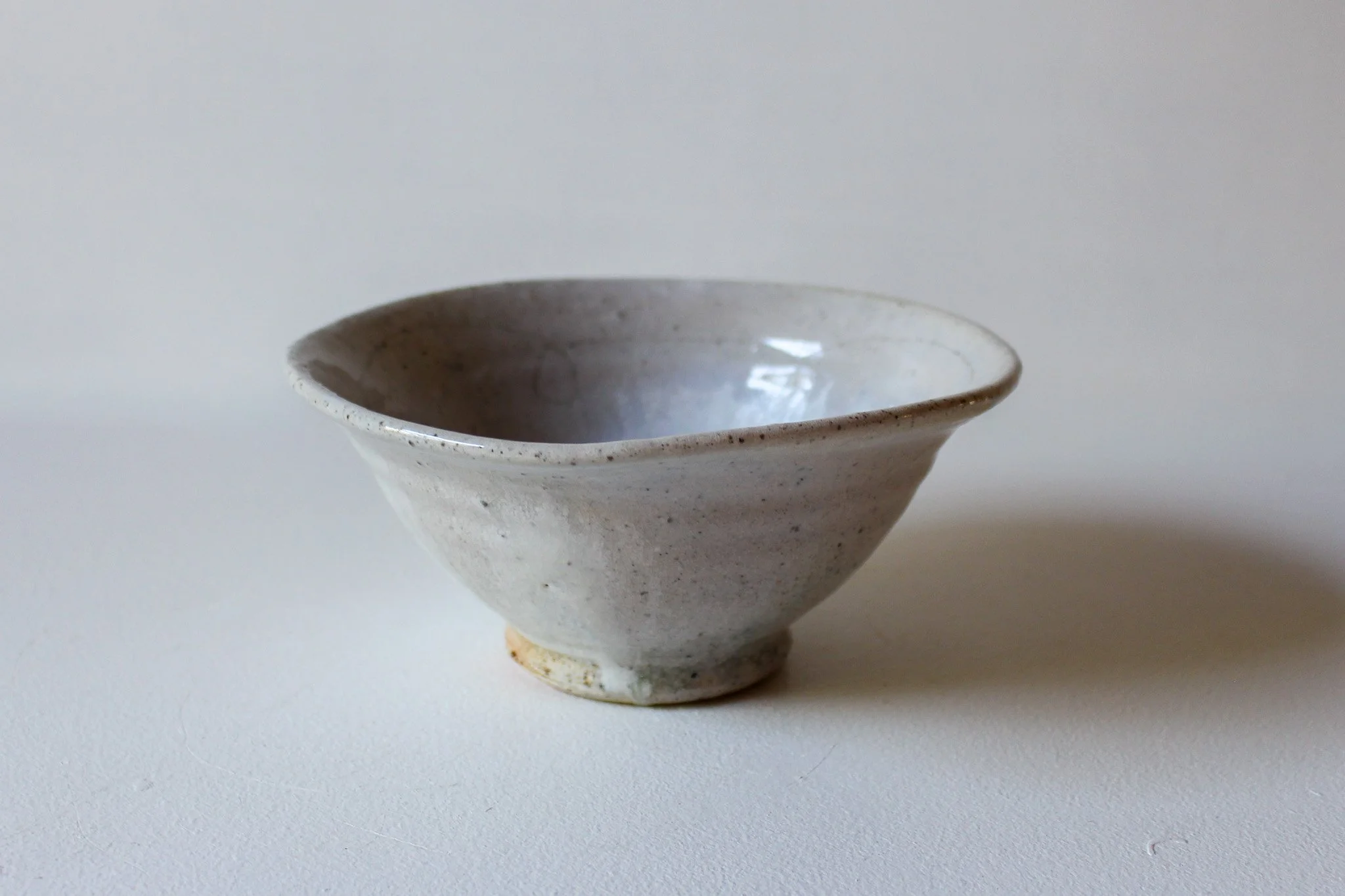 White ceramic bowl with speckled glaze, shallow and wide, placed on a plain white surface with a neutral background.