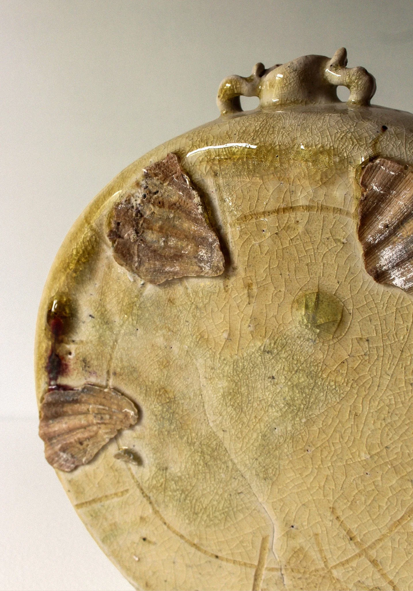 Close-up of a decorative ceramic object with a cracked, aged glaze, featuring small clay pieces attached on the surface.