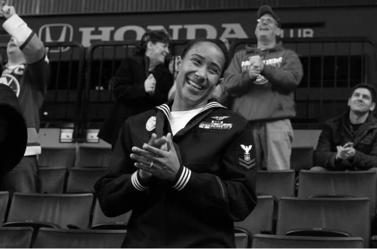 Smiling woman in navy uniform clapping in a stadium with other spectators around her.