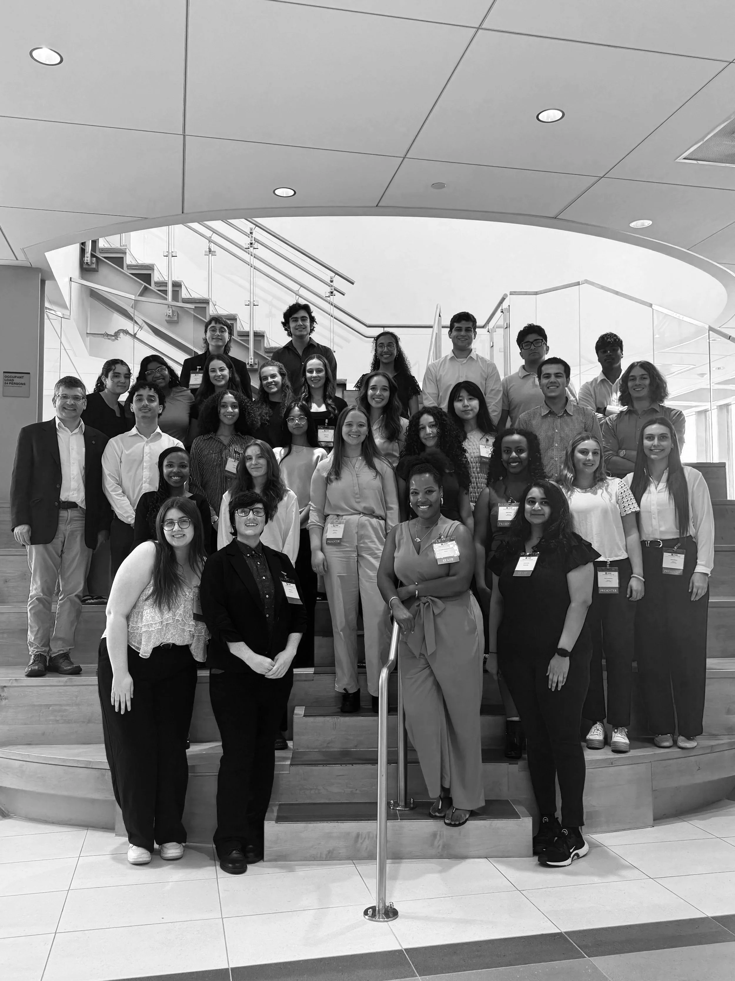 Group of diverse people posing on stairs in an indoor modern building with curved ceiling. Photo from the Aresty Research Center at Rutgers University New Brunswick