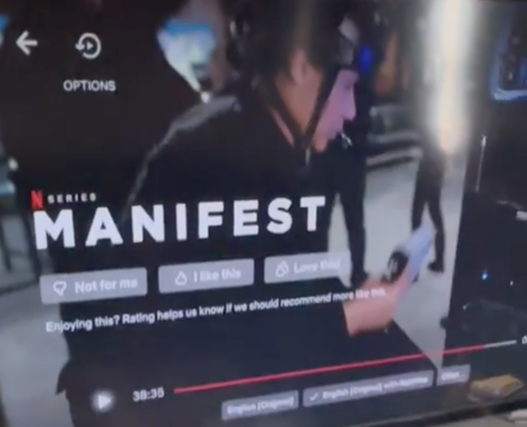 Screen capture of a Netflix series titled 'Manifest' showing a young man wearing a helmet and holding a phone, with a few foot soldiers visible in the background.