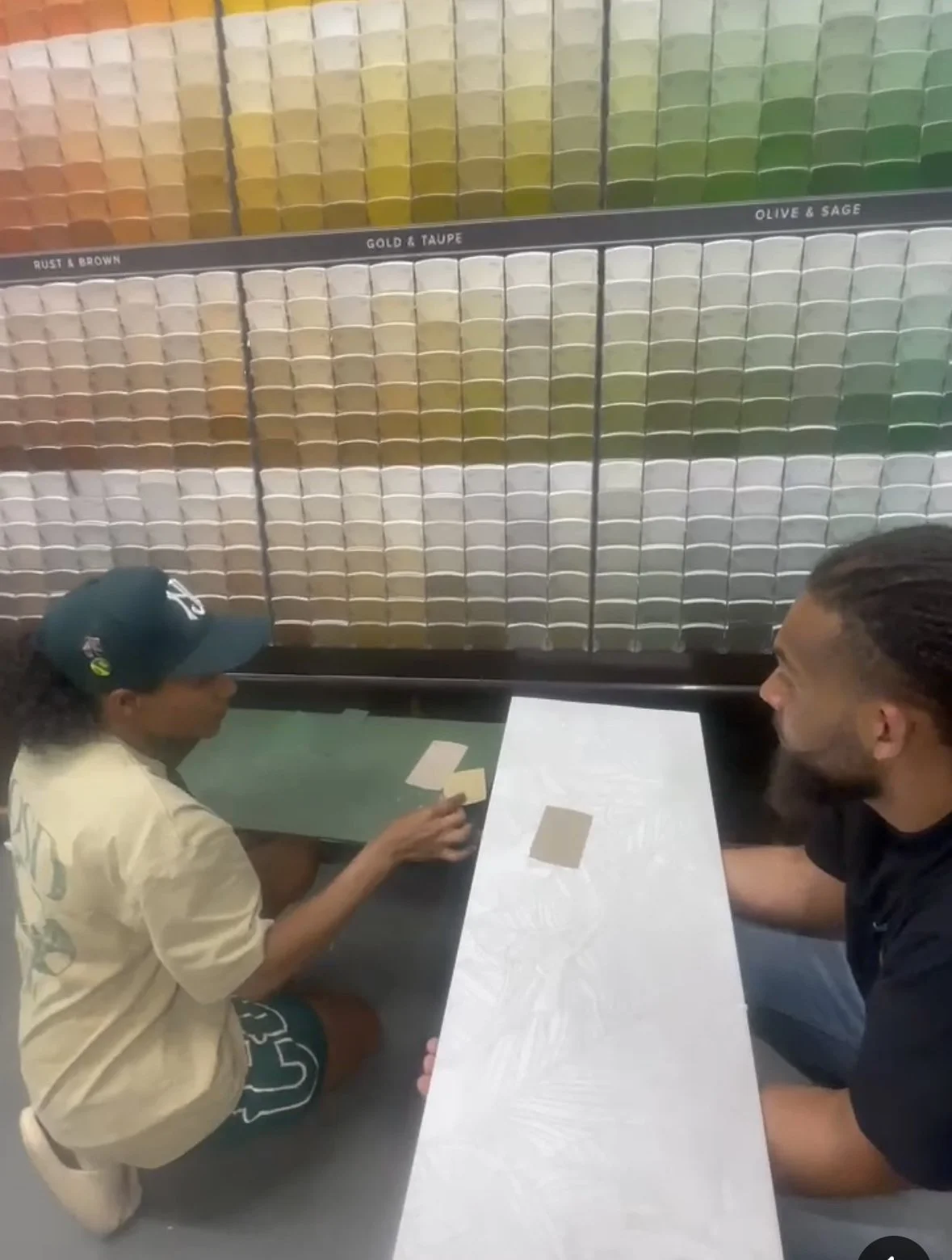 Two people playing a color-matching game at a table, with a display of colored squares in the background labeled by color groups.
