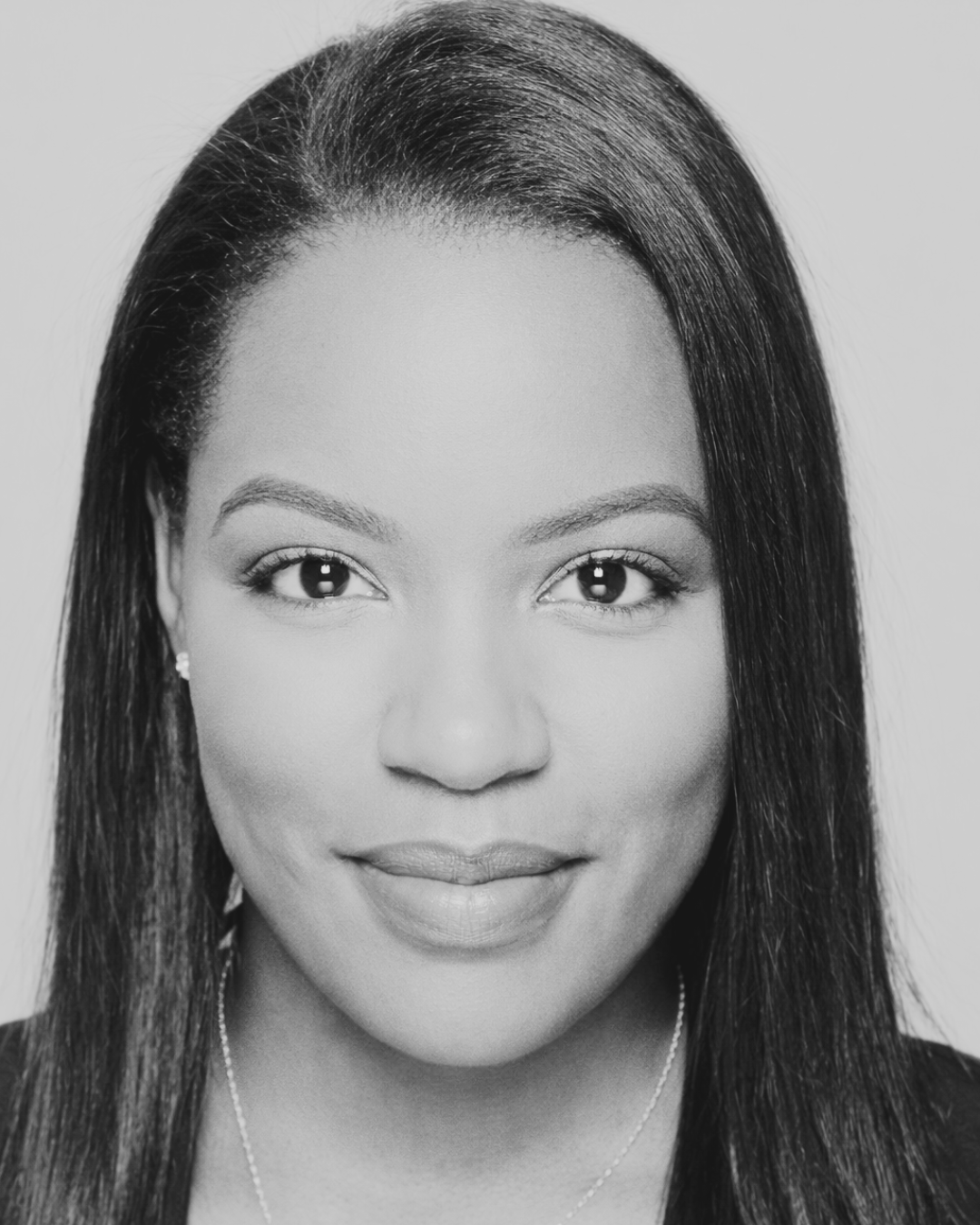Black and white portrait of a woman with straight hair, smiling softly, wearing earrings and a necklace. Dr. Tamiah Brevard-Rodriguez aka Dr. Beauty