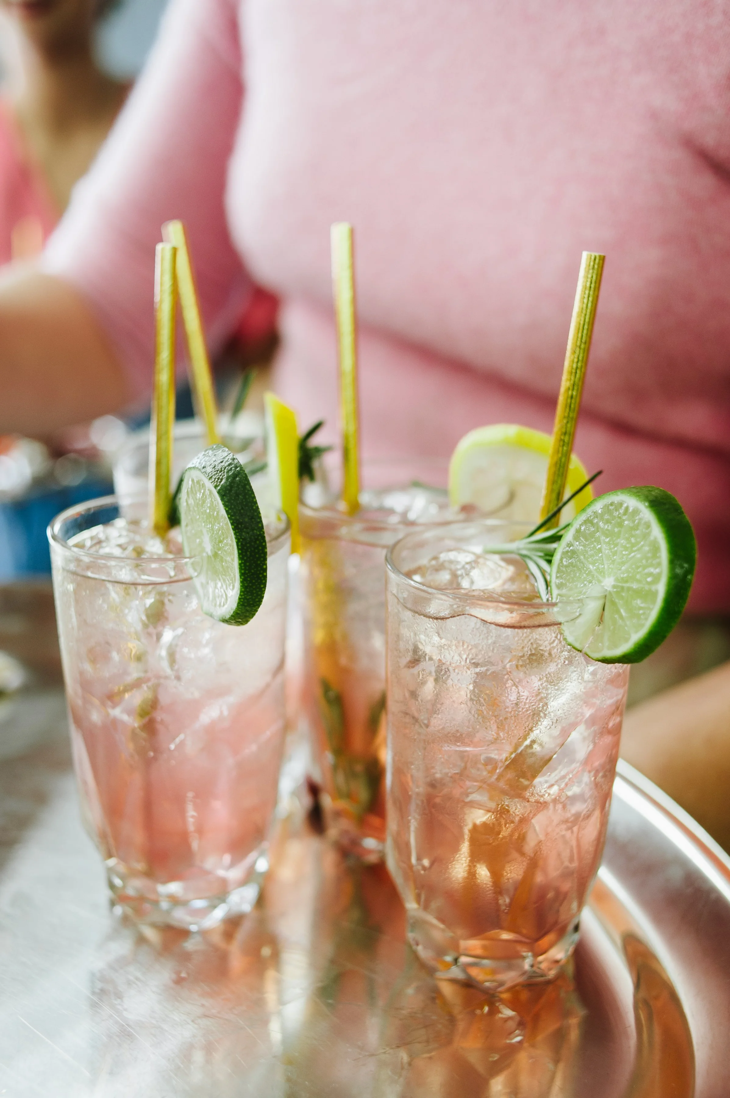 Three glasses of pink lemonade garnished with lime slices and lemon wedges on a silver tray.