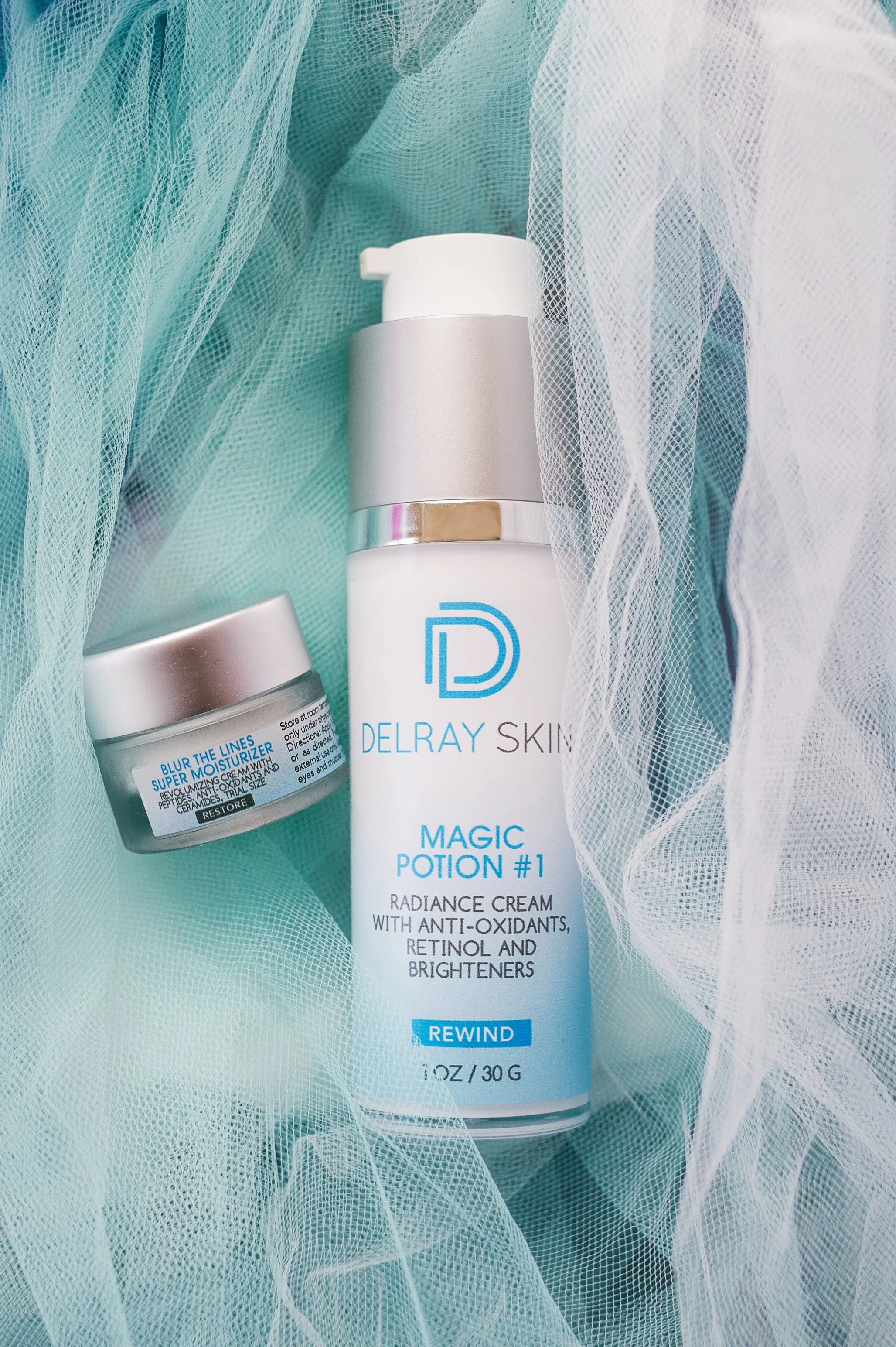 Delray Skin Magic Potion #1 radiance cream and another skincare jar surrounded by light blue and white tulle fabric.