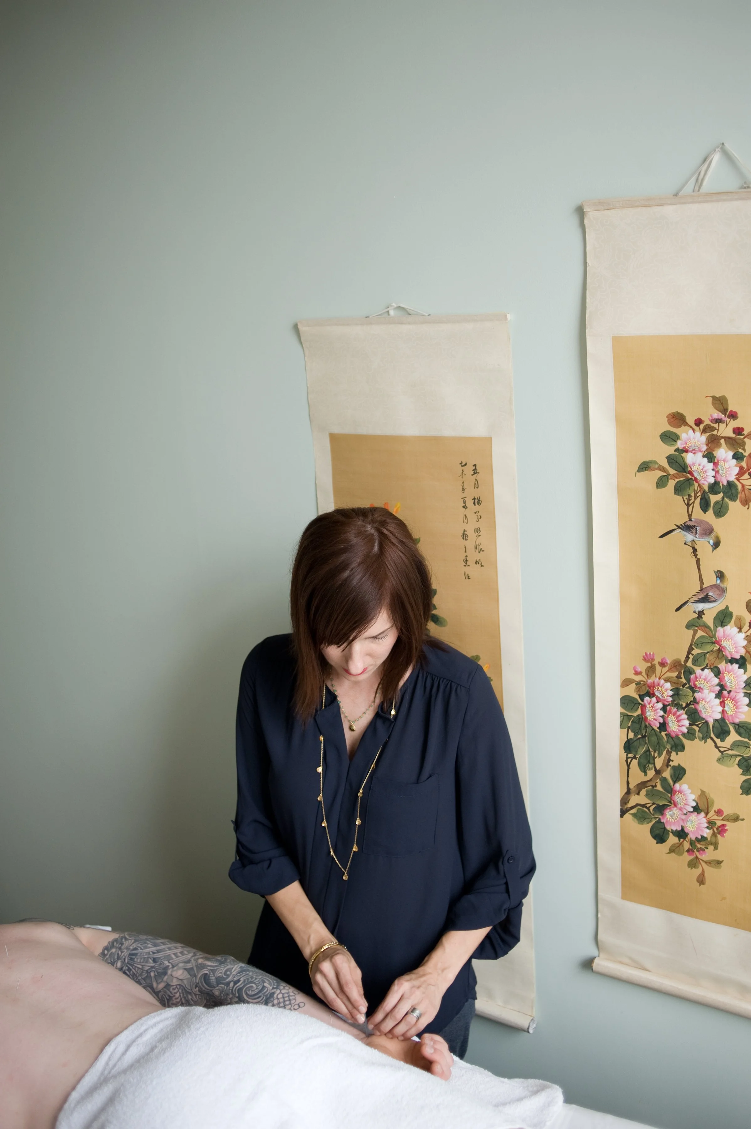 Woman receiving acupuncture treatment on her back in a treatment room decorated with Asian art scrolls.