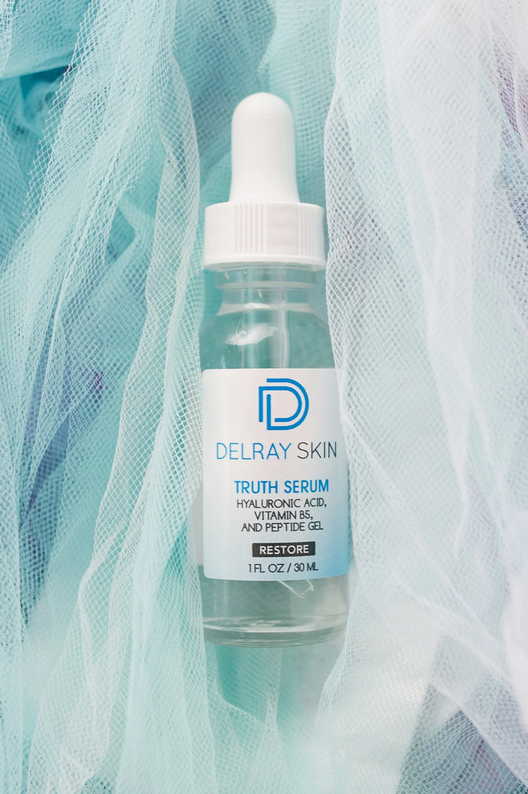 A bottle of Delray Skin Truth Serum surrounded by light blue and white fabric.