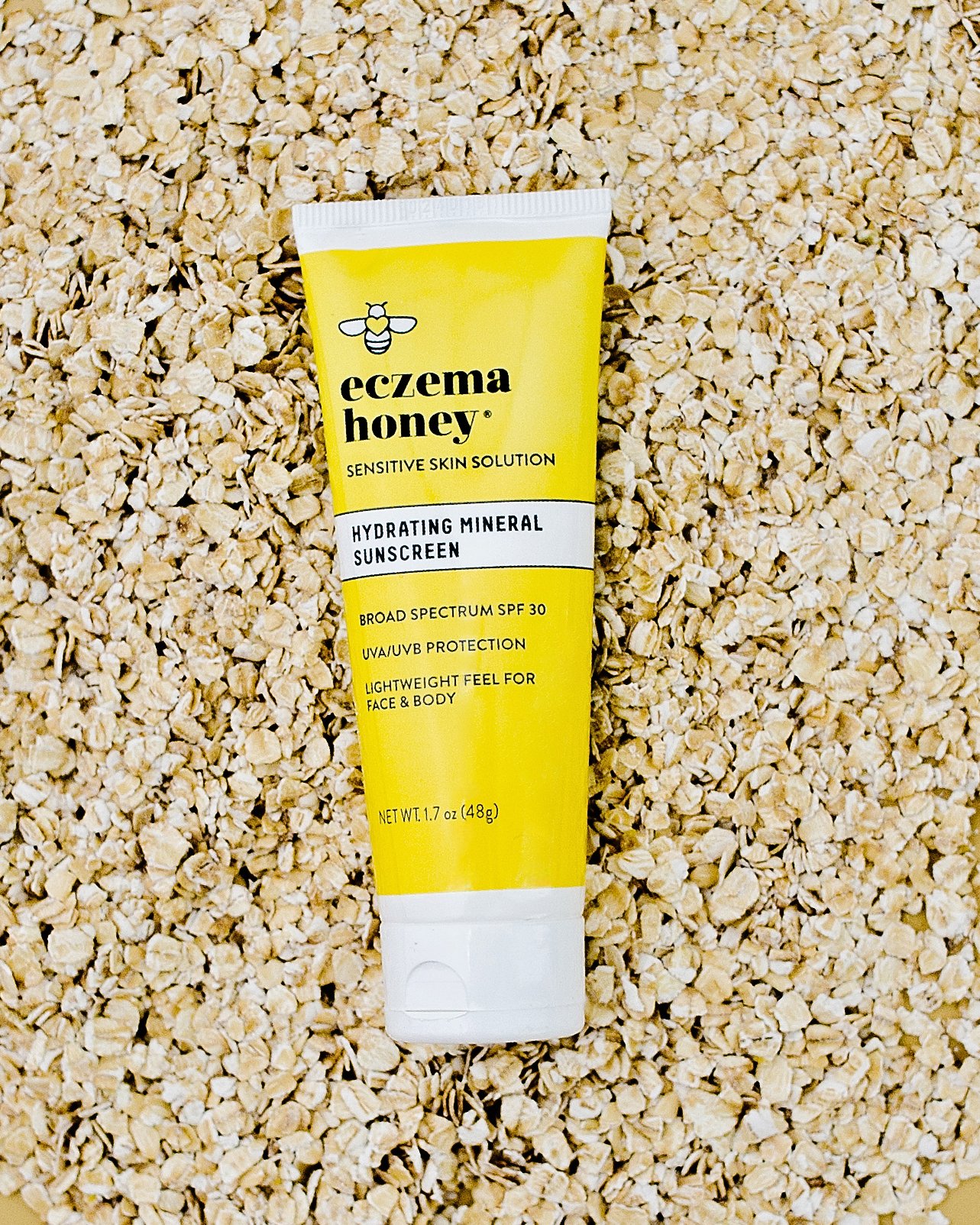 A tube of eczema honey sensitive skin solution hydrating mineral sunscreen with broad spectrum SPF 30 resting on a bed of oatmeal flakes.