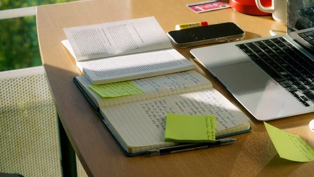 open notebook with pen, sticky notes next to open book, to take notes on reading