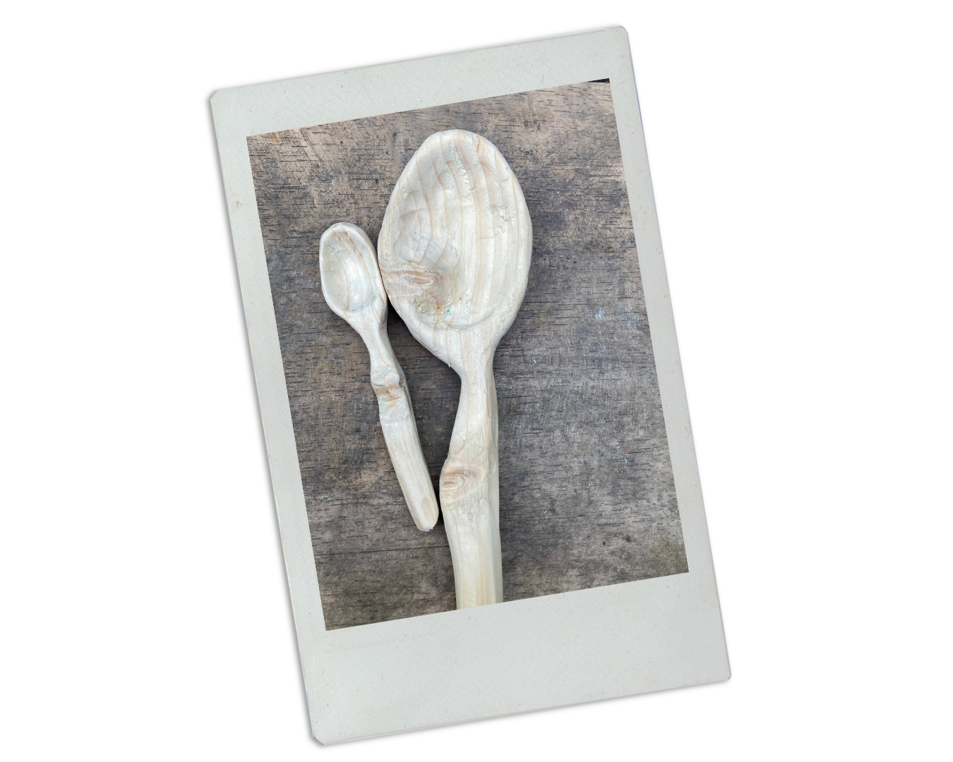 Two wooden spoons on a wooden surface, one large and one small, in a Polaroid frame on a black background.