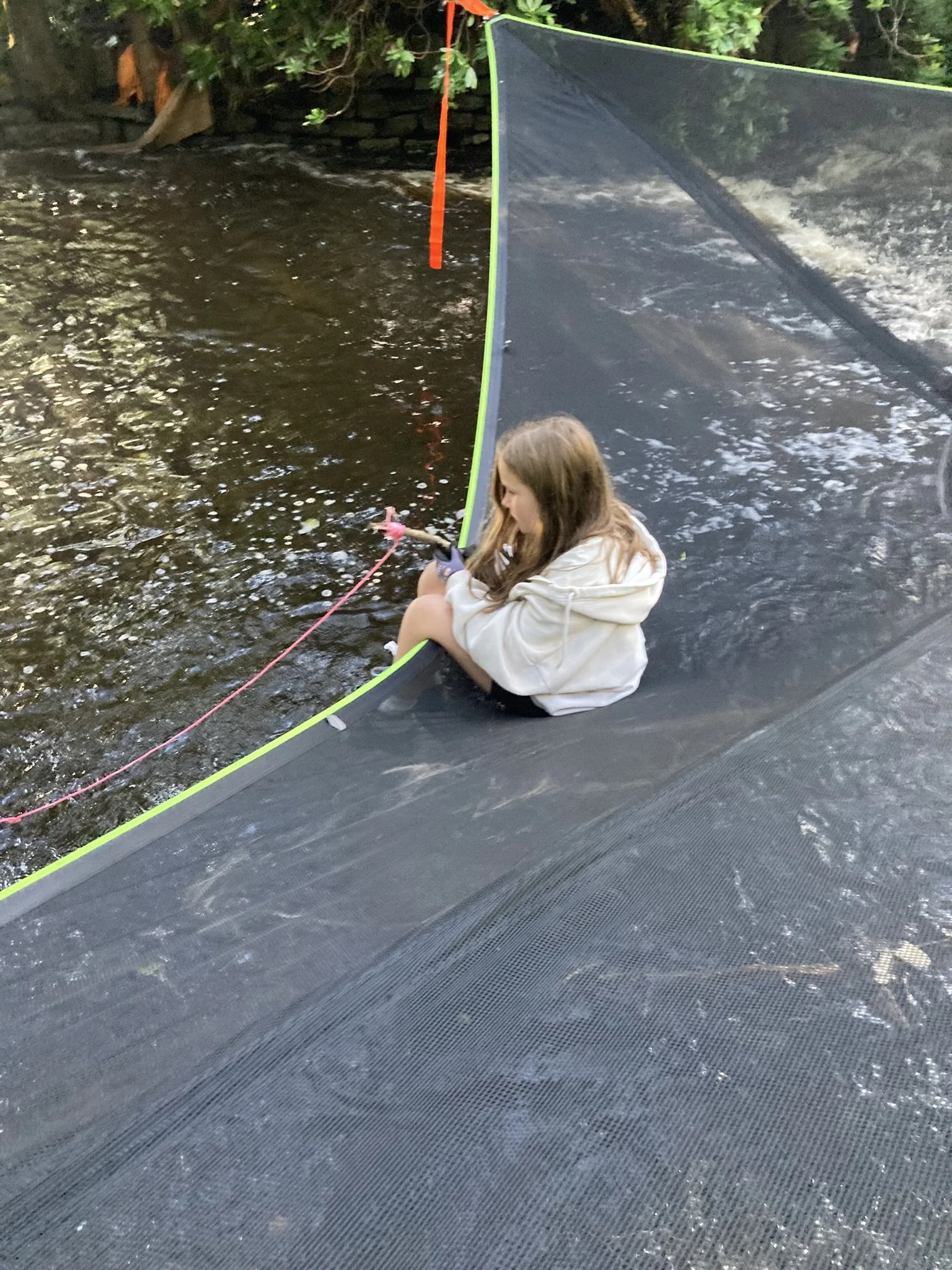 A young girl sitting on the edge of a fishing platform by a body of water, holding a fishing rod.